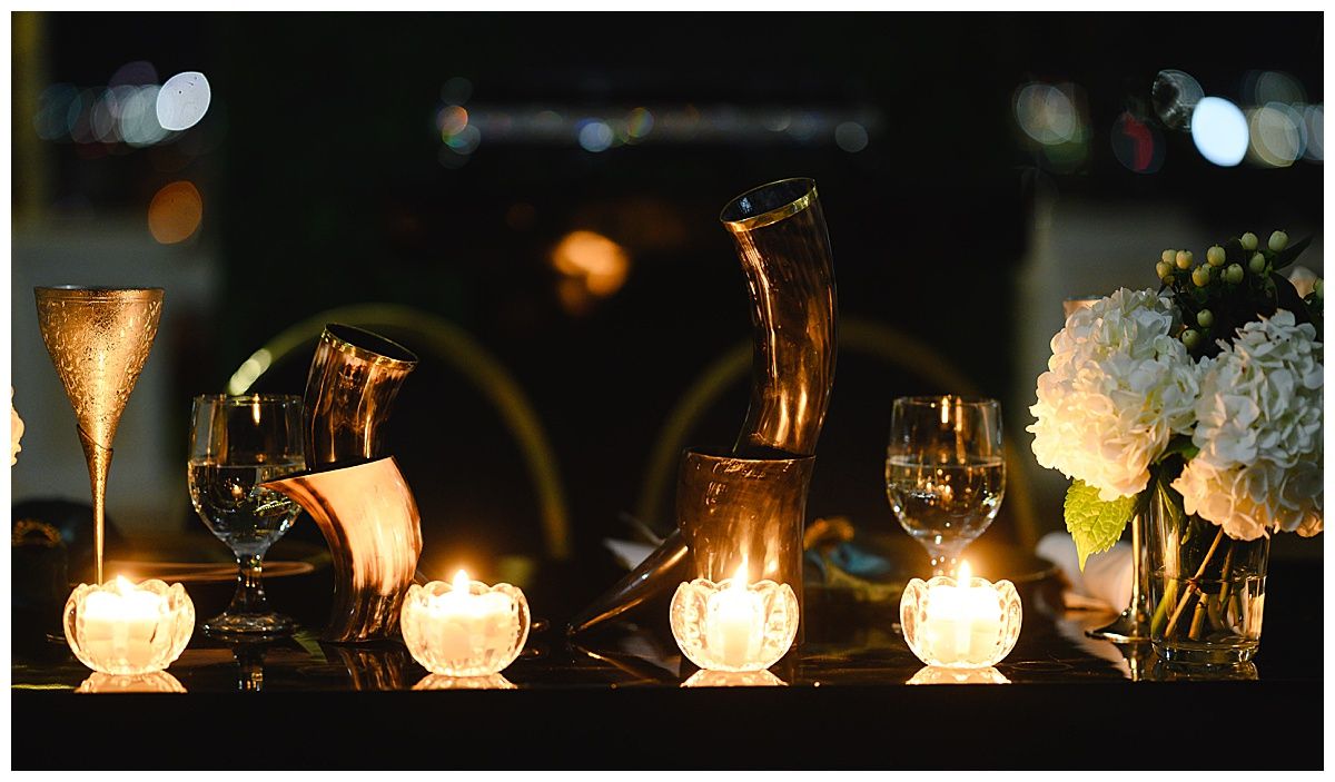 Elegant candlelit table with glowing votives, crystal glasses, and white floral centerpiece in dark romantic setting.