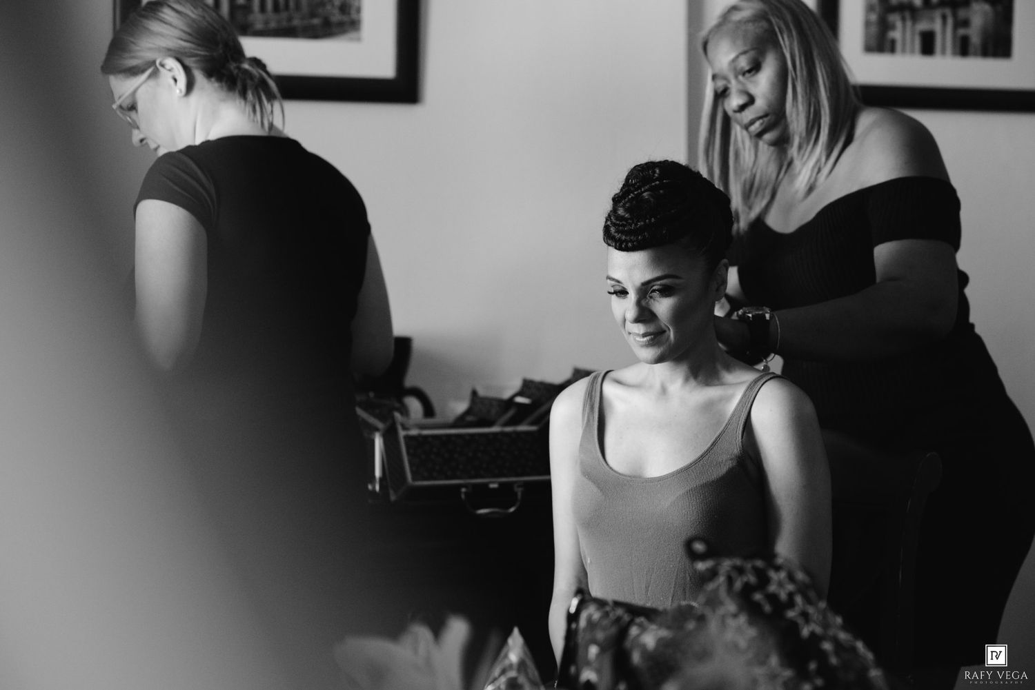Black and white photo of a bride getting hair and makeup done by two stylists before her wedding ceremony.