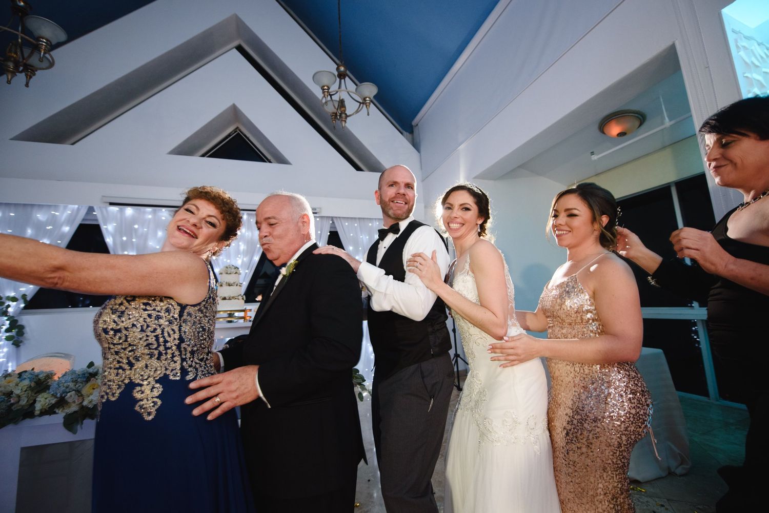 Wedding party taking a selfie with bride in white gown and guests in formal attire at elegant indoor venue.