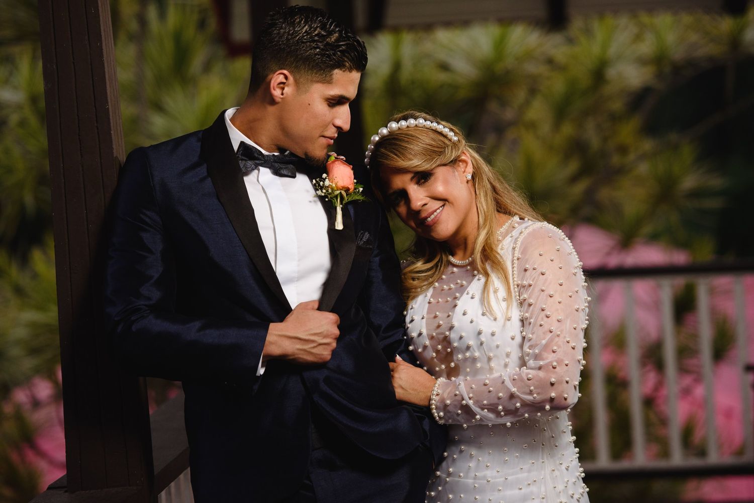 Bride in pearl wedding gown and groom in navy tuxedo share a tender moment outdoors.