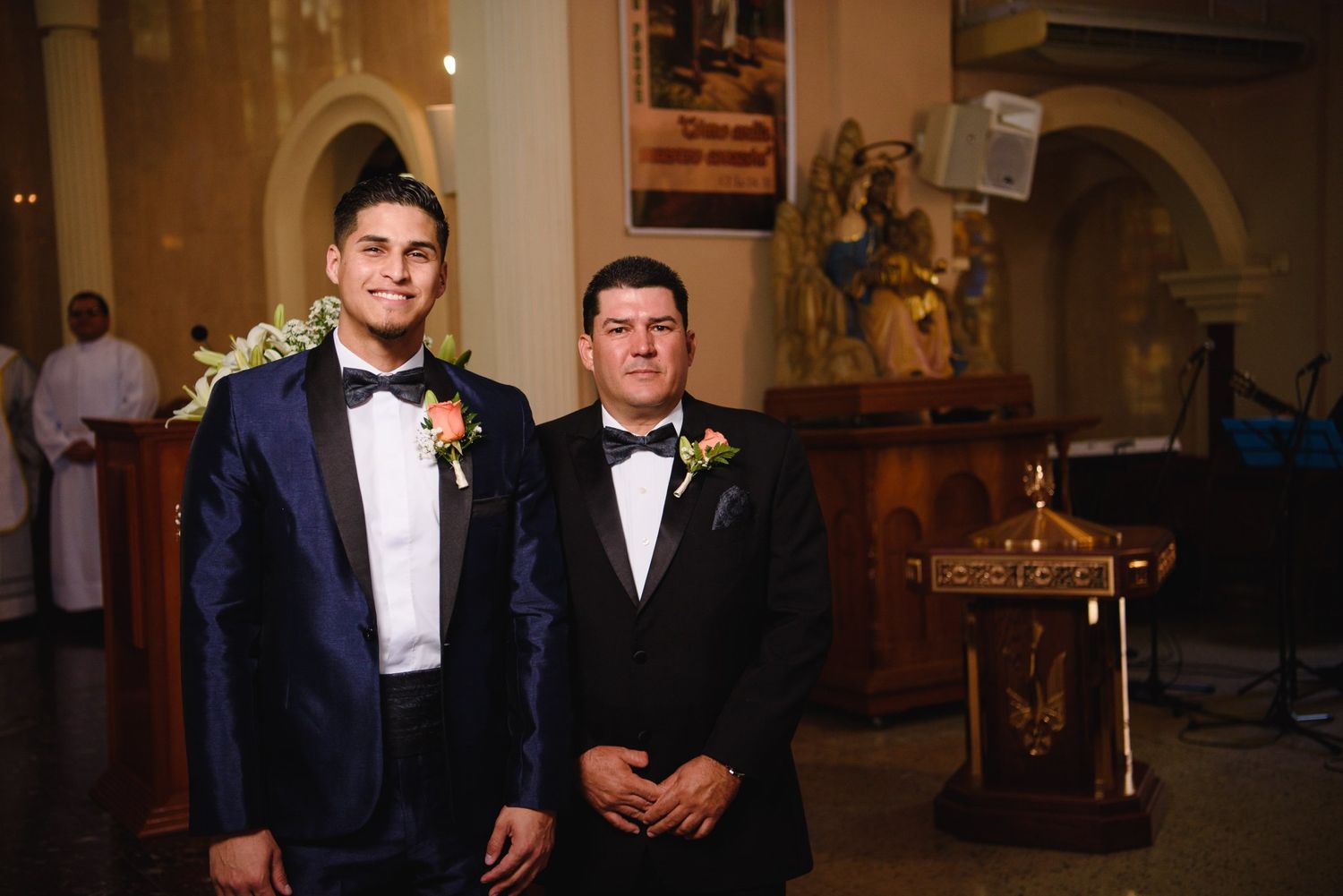 Two grooms in tuxedos stand at the altar of a decorated church during a wedding ceremony.