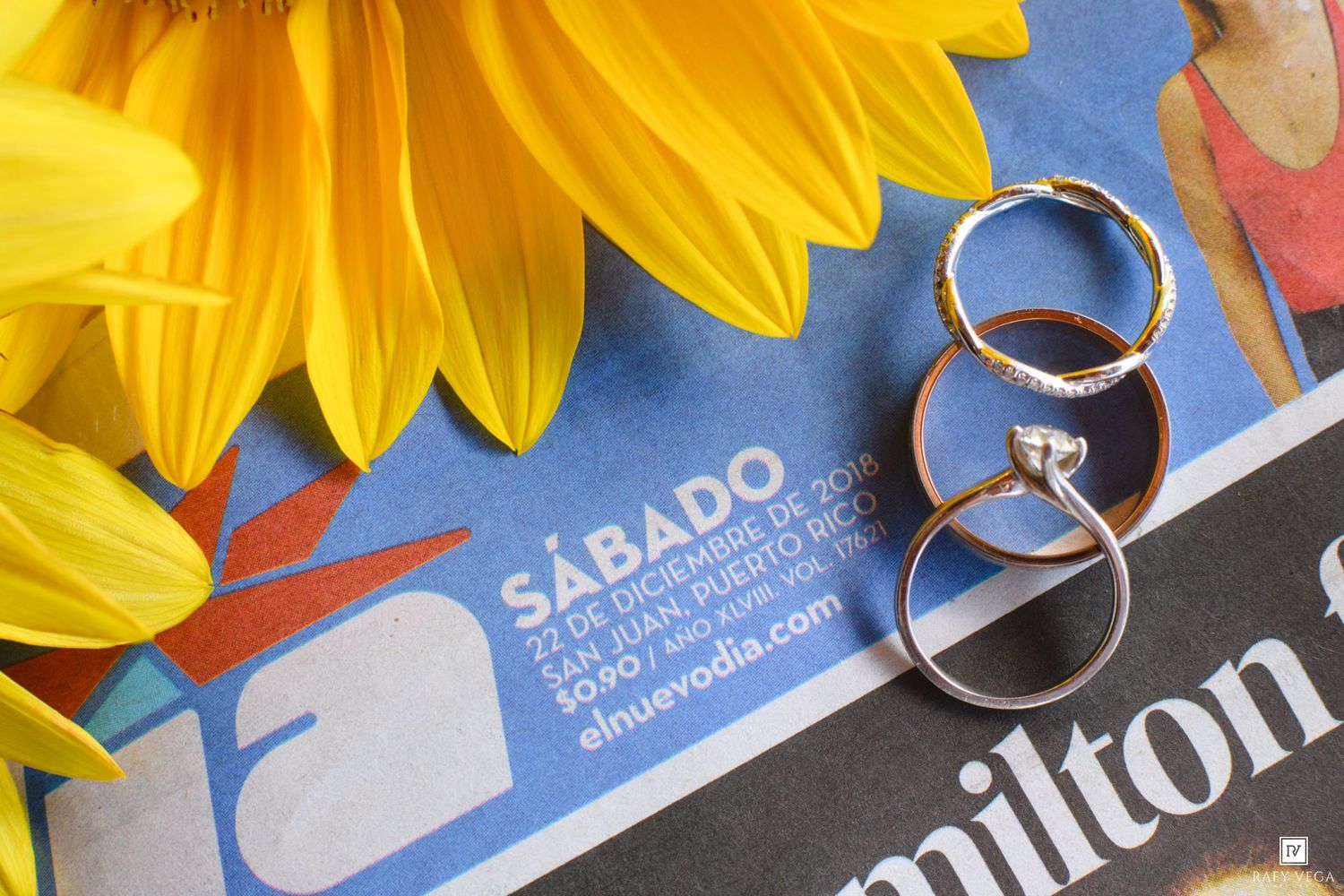 Wedding rings and engagement ring displayed on a Spanish newspaper beside yellow sunflowers.