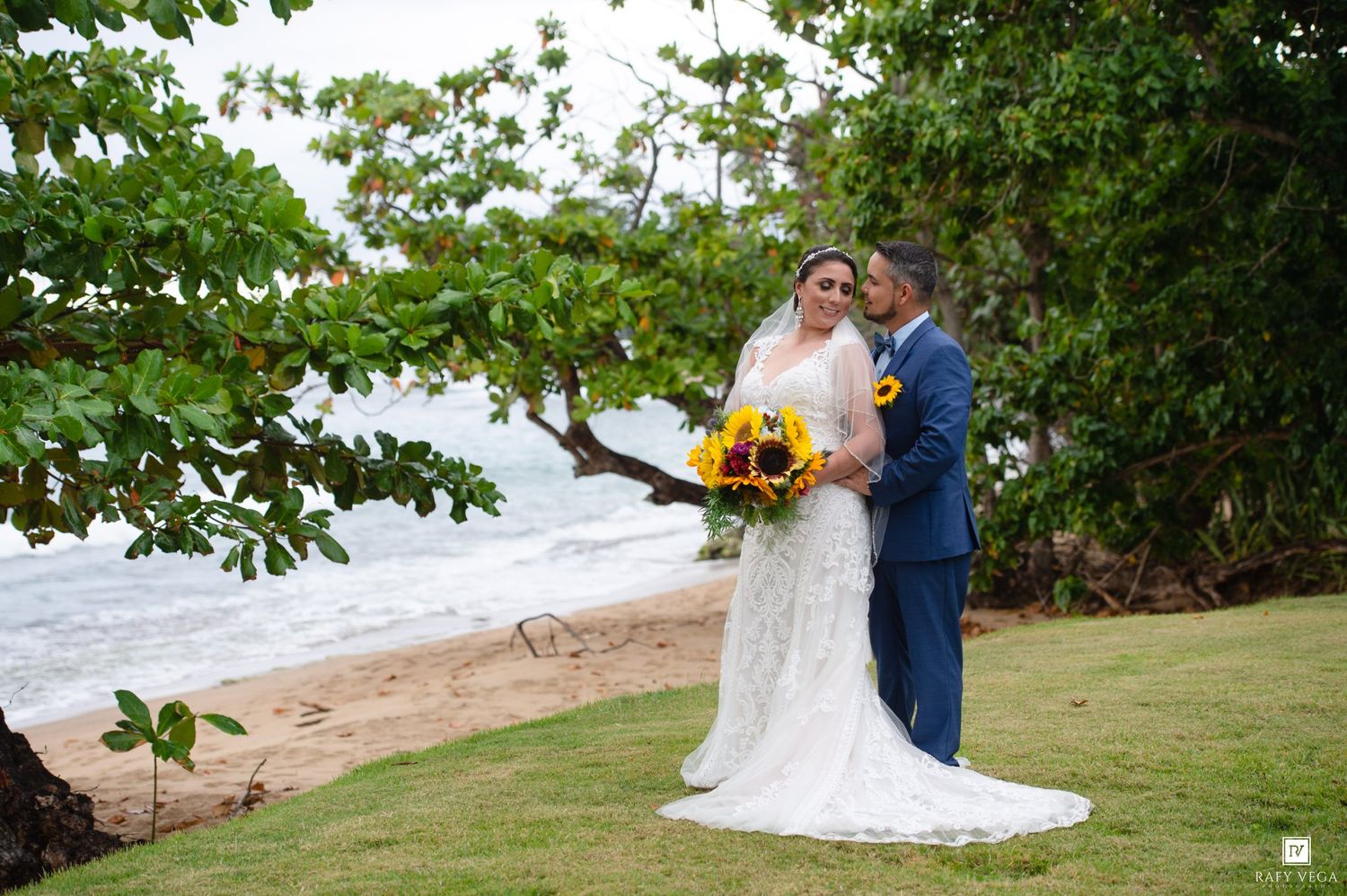 A bride and groom pose romantically on a tropical beach with sunflower bouquet on their wedding day.