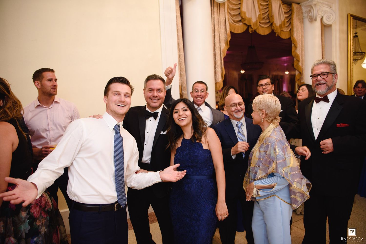 Guests smiling and posing together at an elegant formal event or wedding reception in a grand ballroom.
