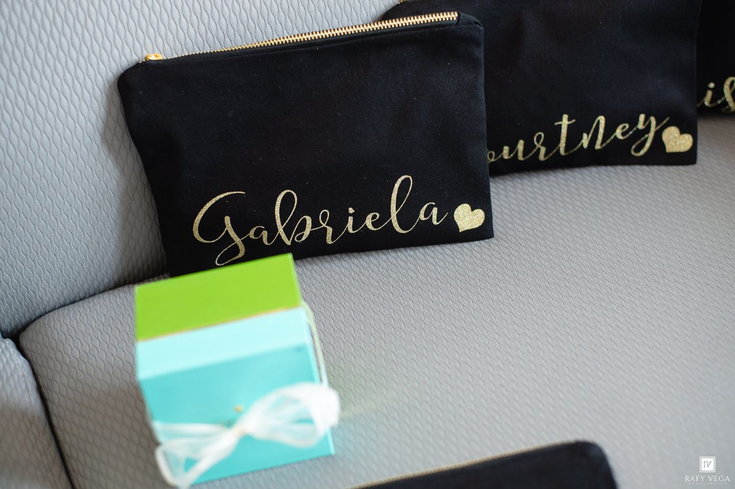Personalized black makeup bags with gold script names Gabriela and Courtney, displayed with a teal gift box.
