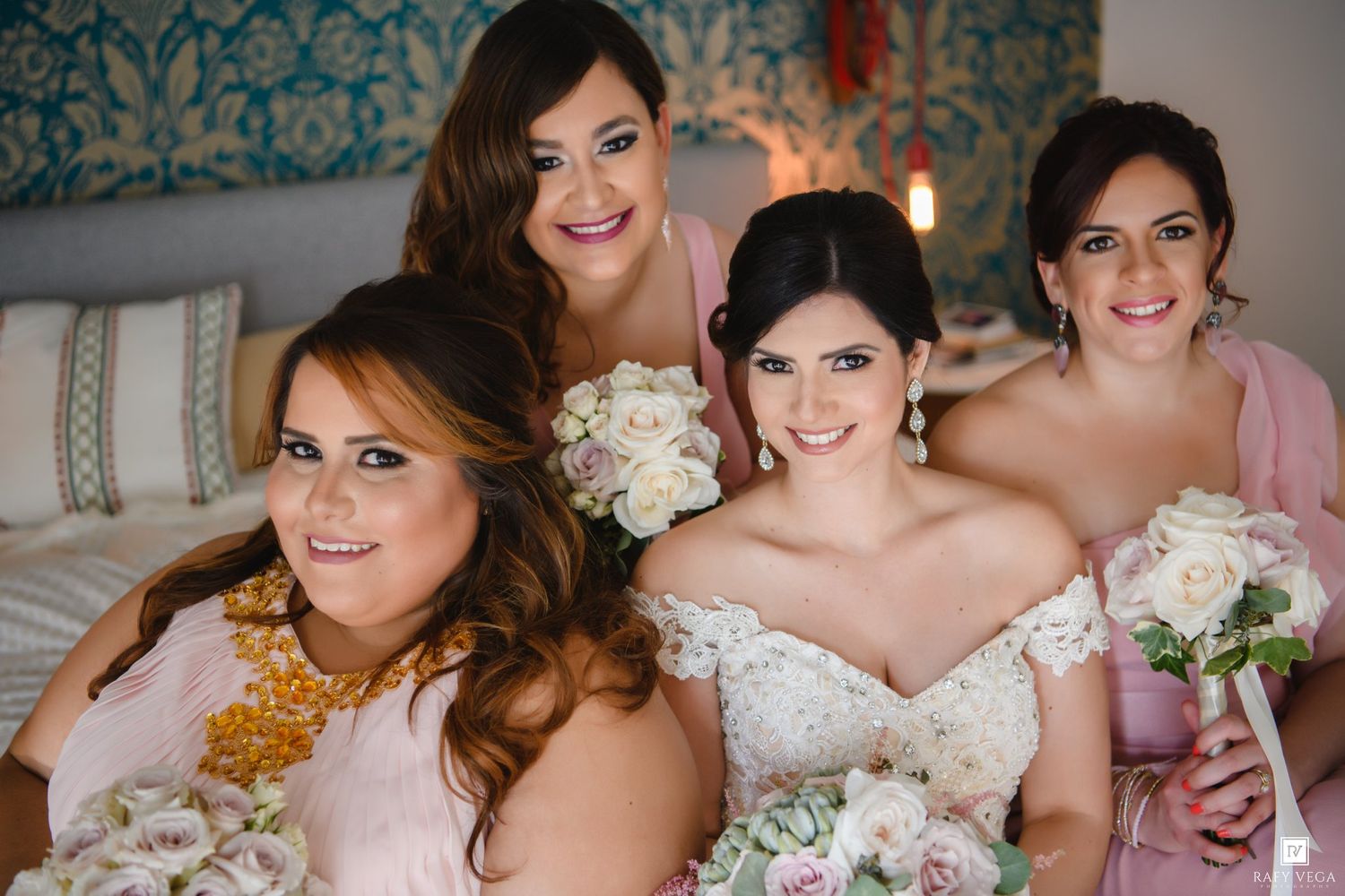 Bride in white gown poses with three bridesmaids in pink dresses holding floral bouquets.