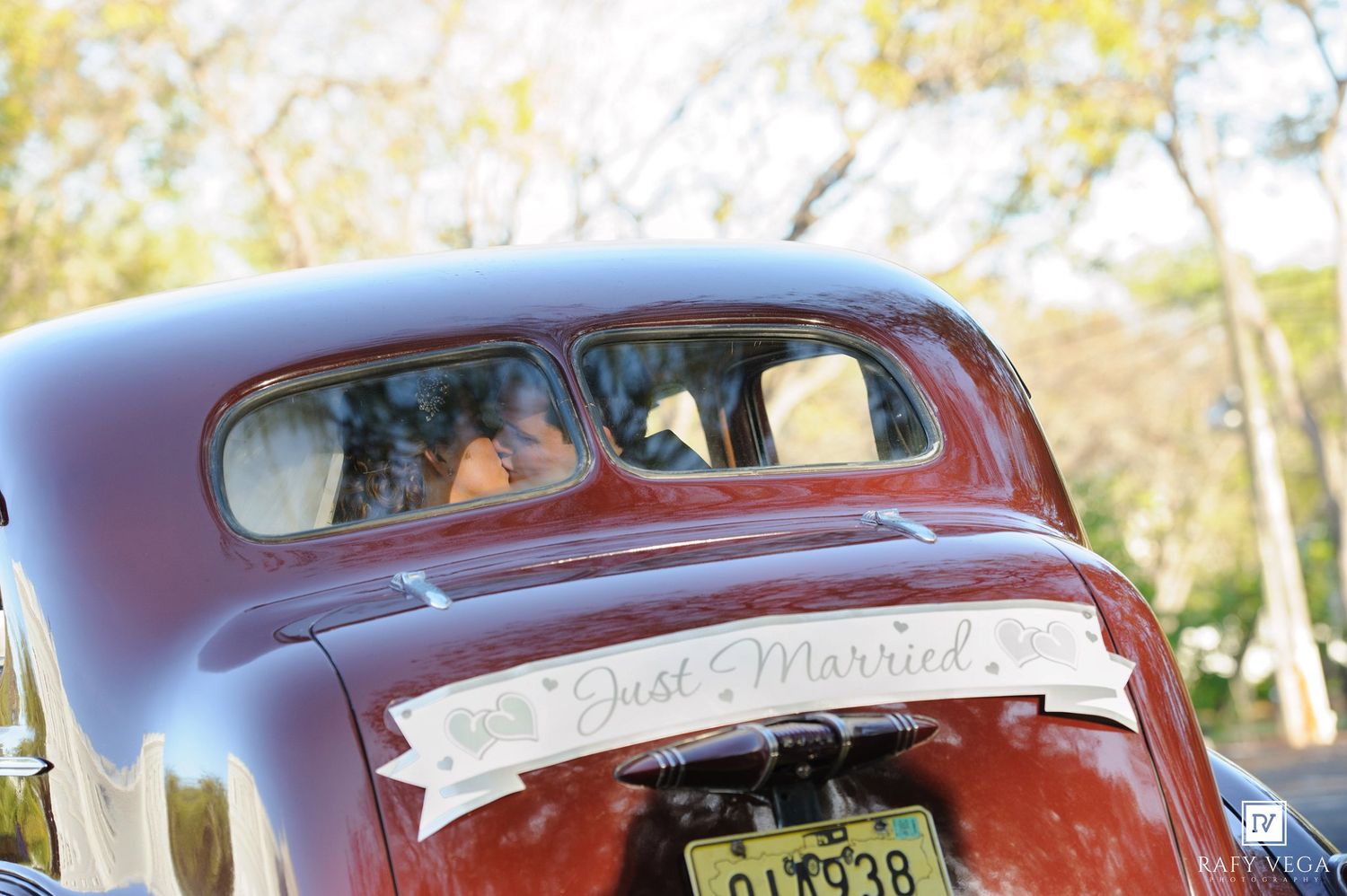 Vintage red just married car with newlyweds visible through rear window on sunny wedding day.