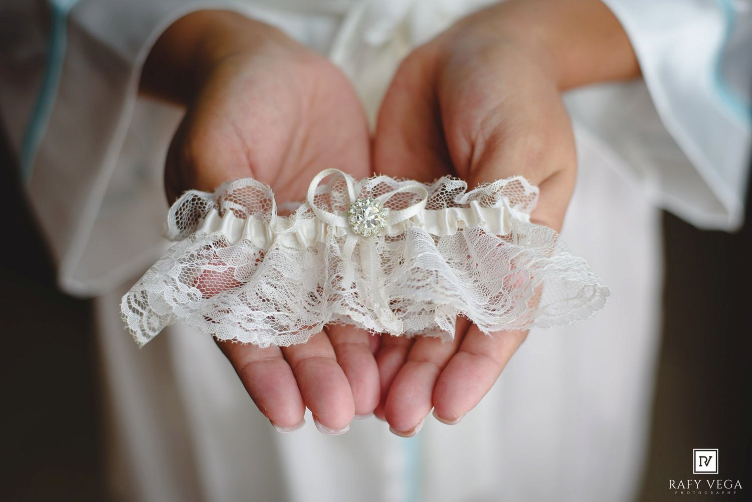 Bride holding a delicate white lace wedding garter with pearl and crystal embellishments in her cupped hands.