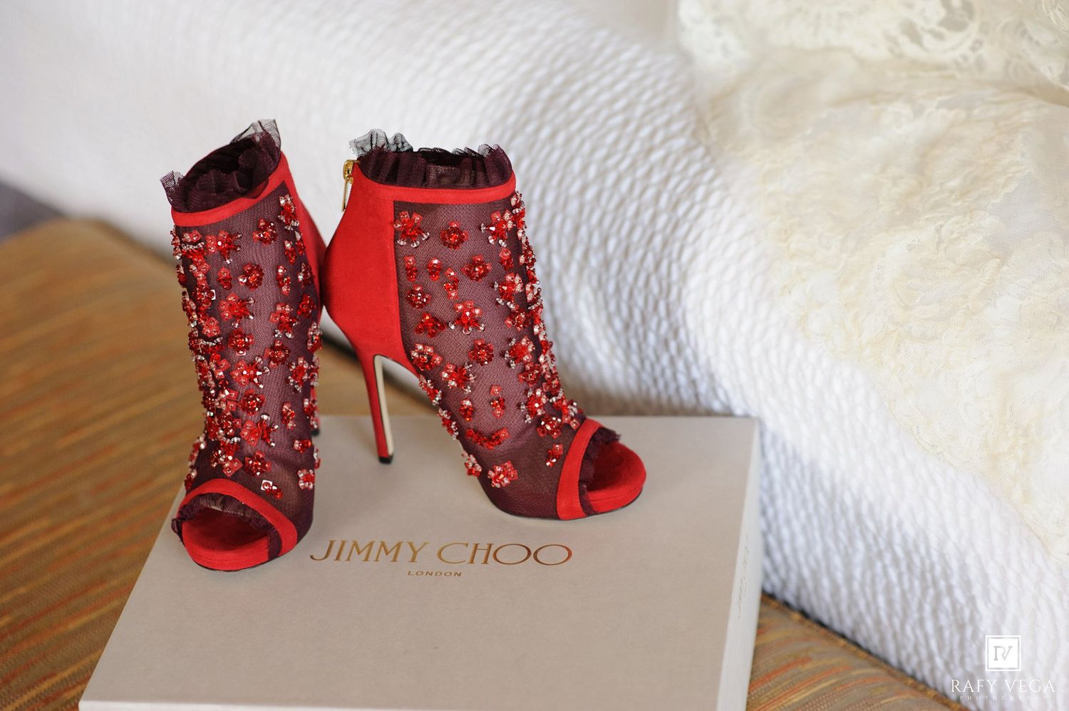 Red Jimmy Choo embellished mesh peep-toe stiletto booties with floral crystal details displayed on branded box.