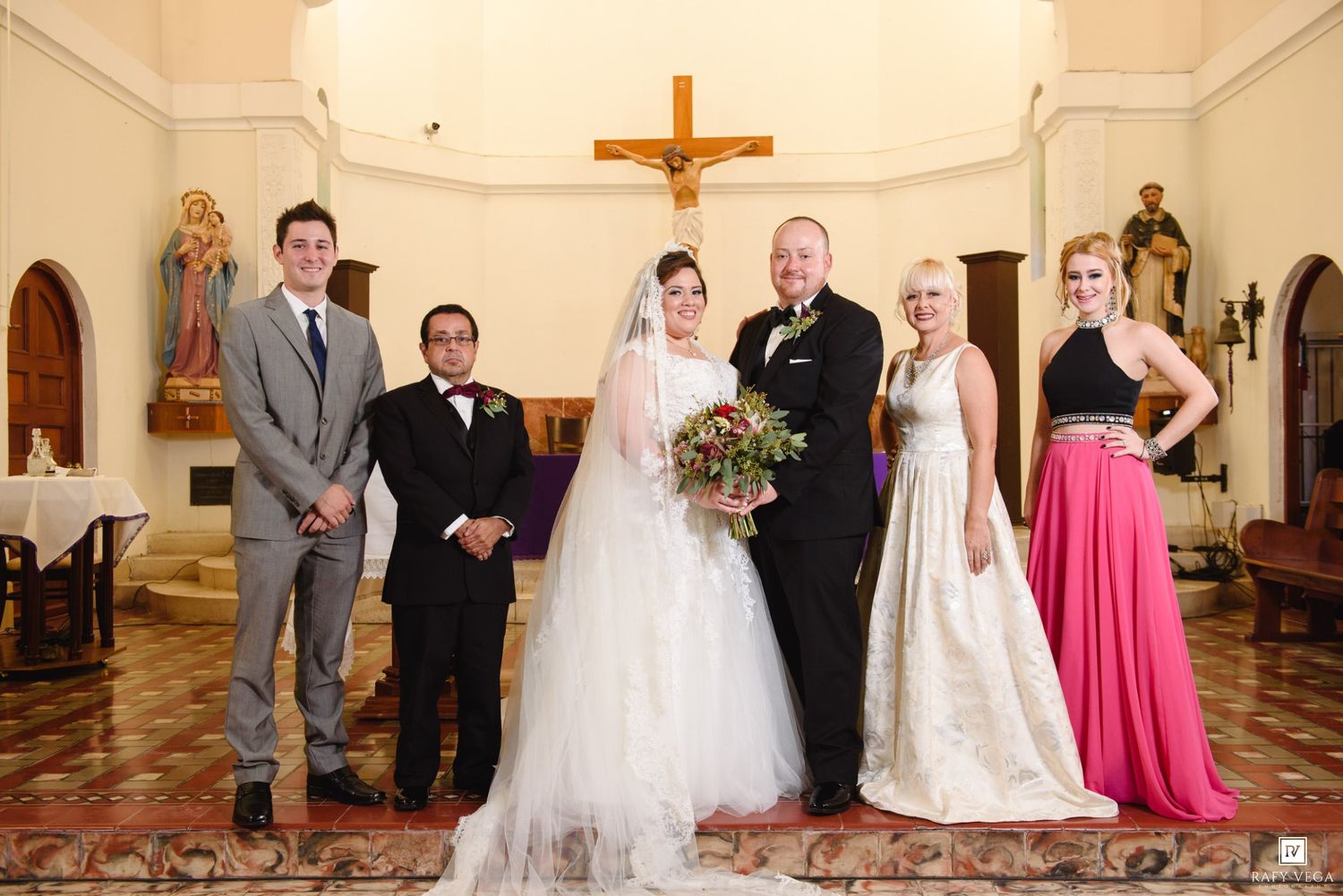 Wedding party poses inside a church with a bride, groom, and four guests in formal attire.