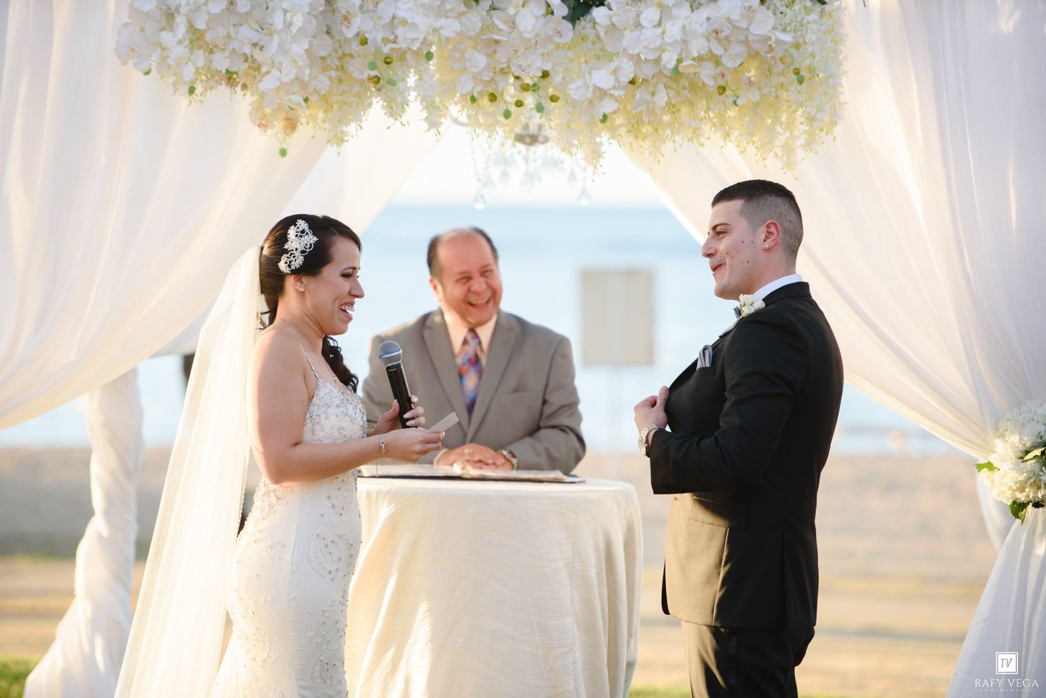 Bride and groom exchange vows under floral arch with officiant at outdoor wedding ceremony.