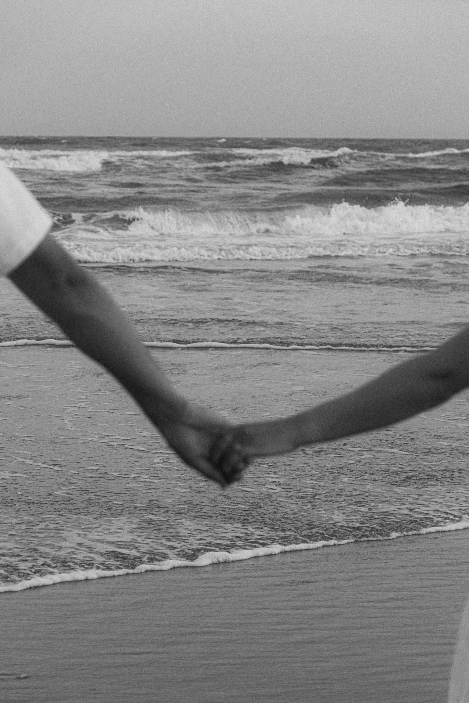 Black and white photo of couple holding hands on beach romantic detail
