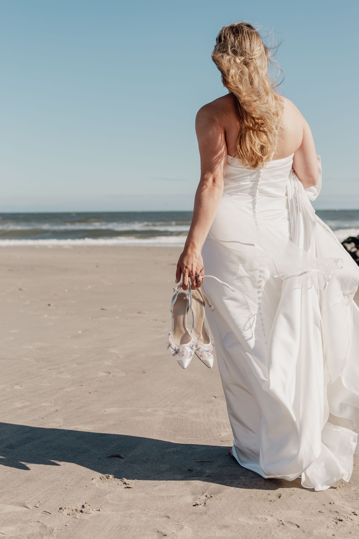Bride walking along shoreline holding dress and shoes South Jersey beach portrait
