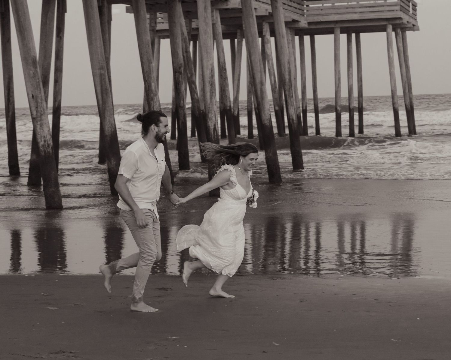 Couple running on beach near pier candid moment South Jersey session