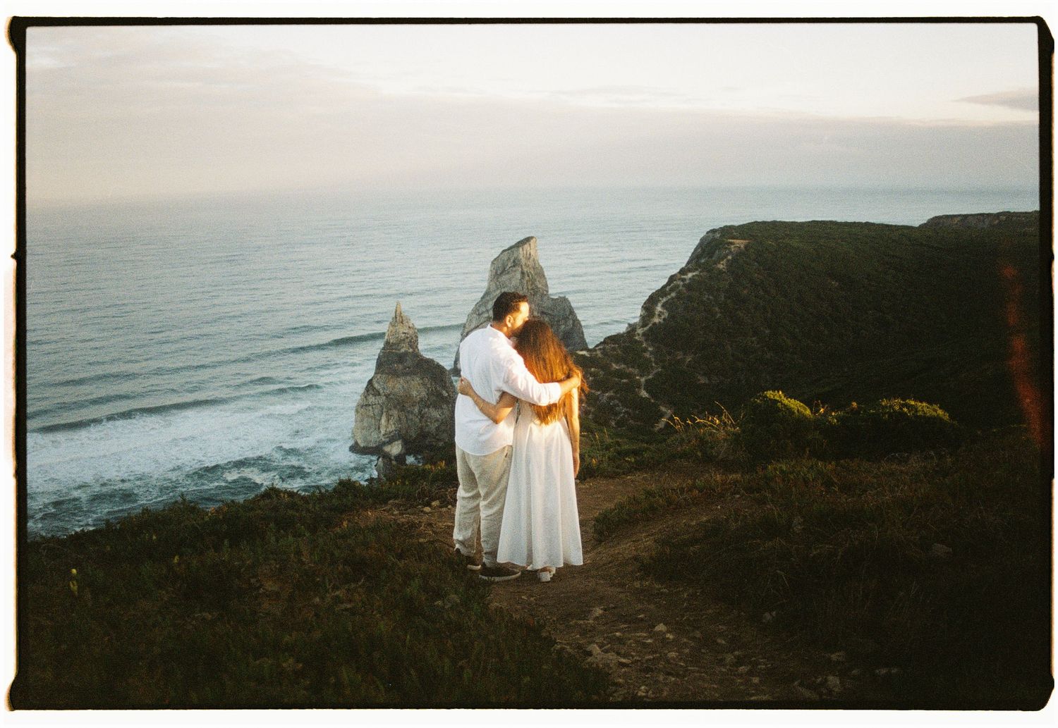 A couple embracing on a clifftop above the Atlantic ocean at sunrise, Praia da Ursa, Portugal