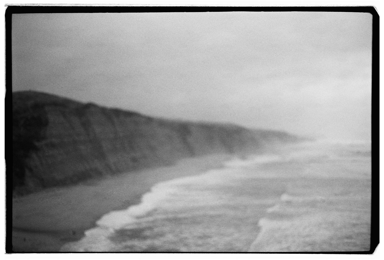 A black and white film photograph of a misty coastal landscape with dramatic cliffs.
