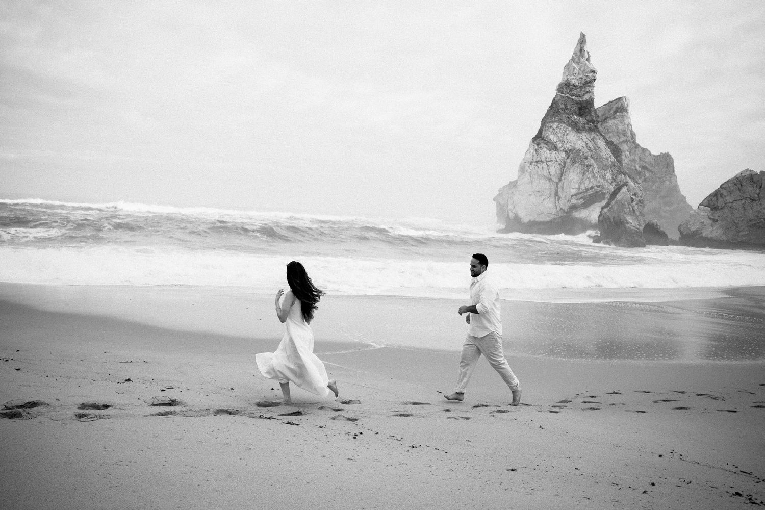 A couple running together on Praia da Ursa with dramatic rock formations behind them, couple photography Portugal