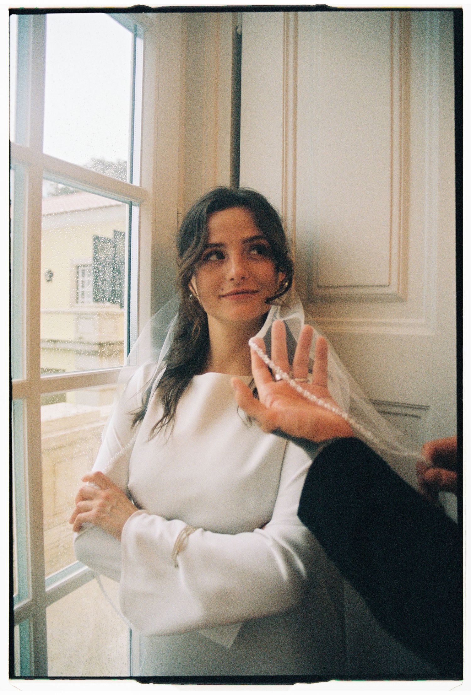 A vintage-style film portrait of a woman standing by a window during an elopement session in Estoril, Portugal