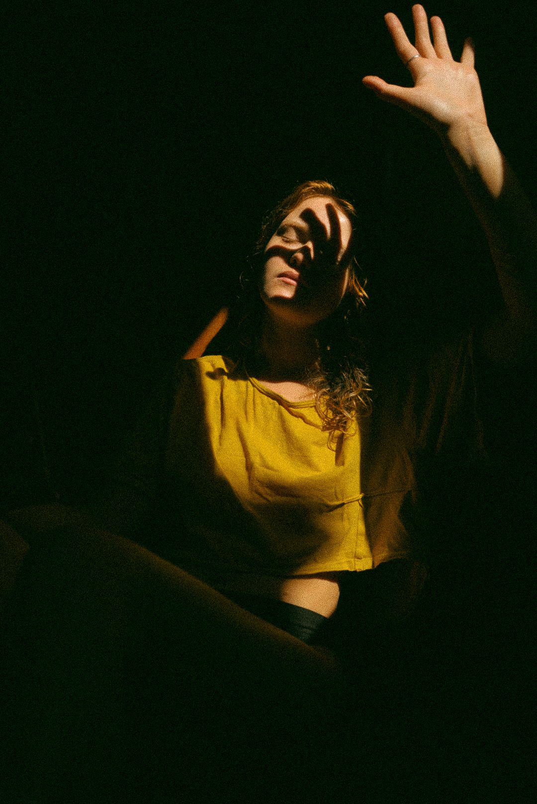 A dramatic portrait of a woman in a yellow dress reaching upward in a dark setting