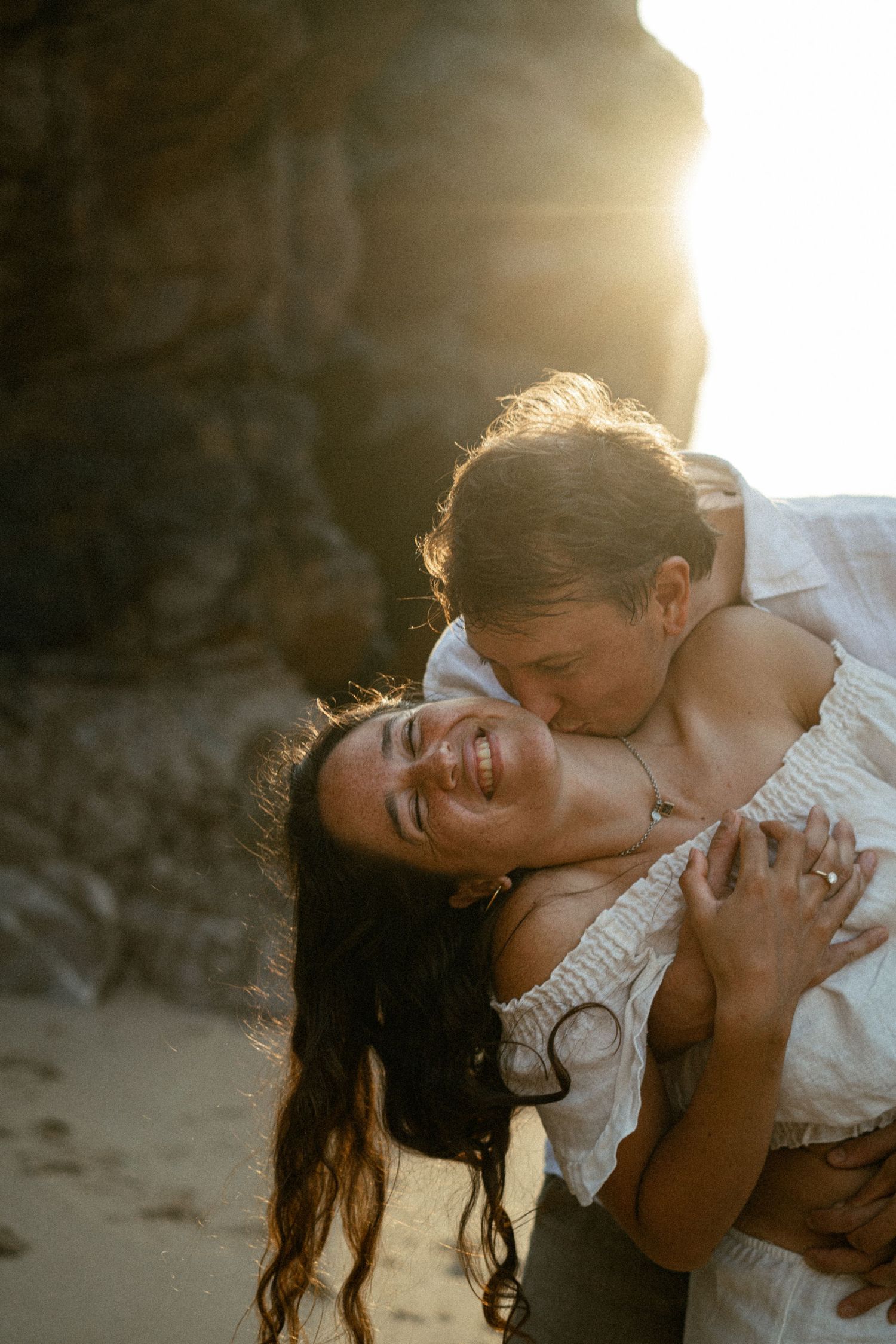 A couple embracing on a beach with golden sunset light streaming through, couples photography Portugal