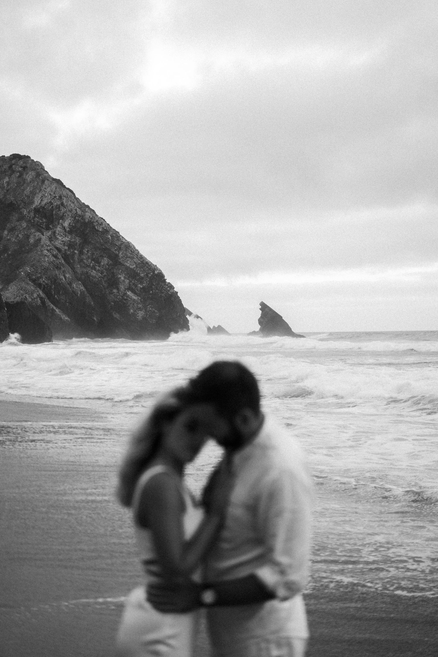 A couple sharing a tender moment on Adraga beach with dramatic rock formations during a couples session in Portugal