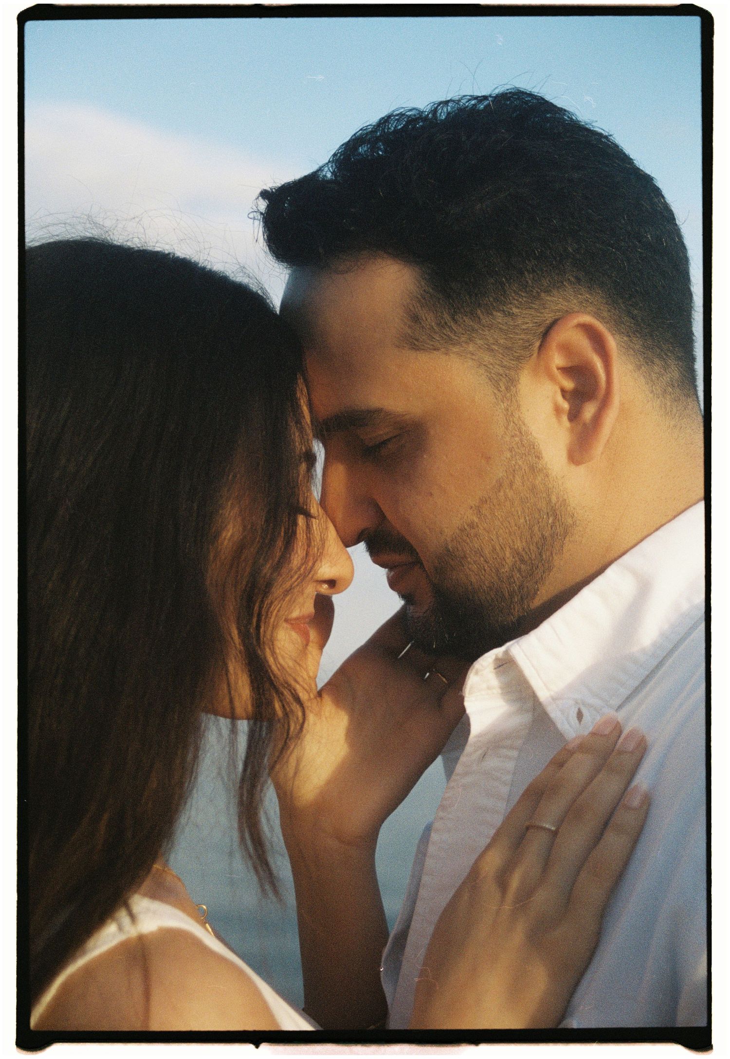 An intimate sunset portrait of a couple in white clothing sharing a romantic moment.