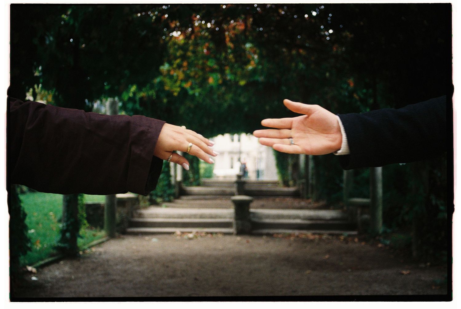 A couple reaching out their hands to each other in a tree-lined garden during the pre-wedding session in Paris