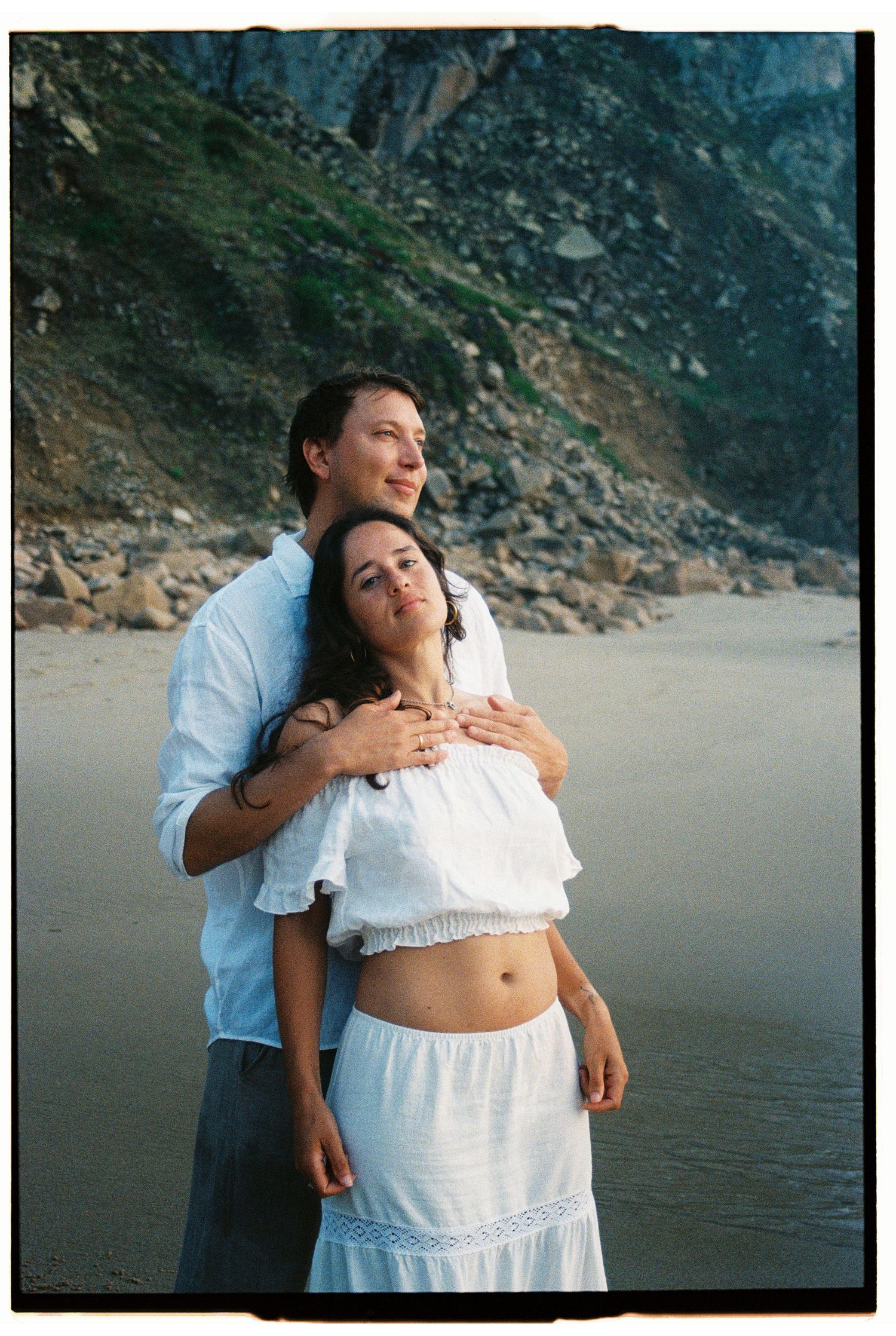 A couple resting together on Praia da Ursa beach with dramatic rock formations behind them, Portugal
