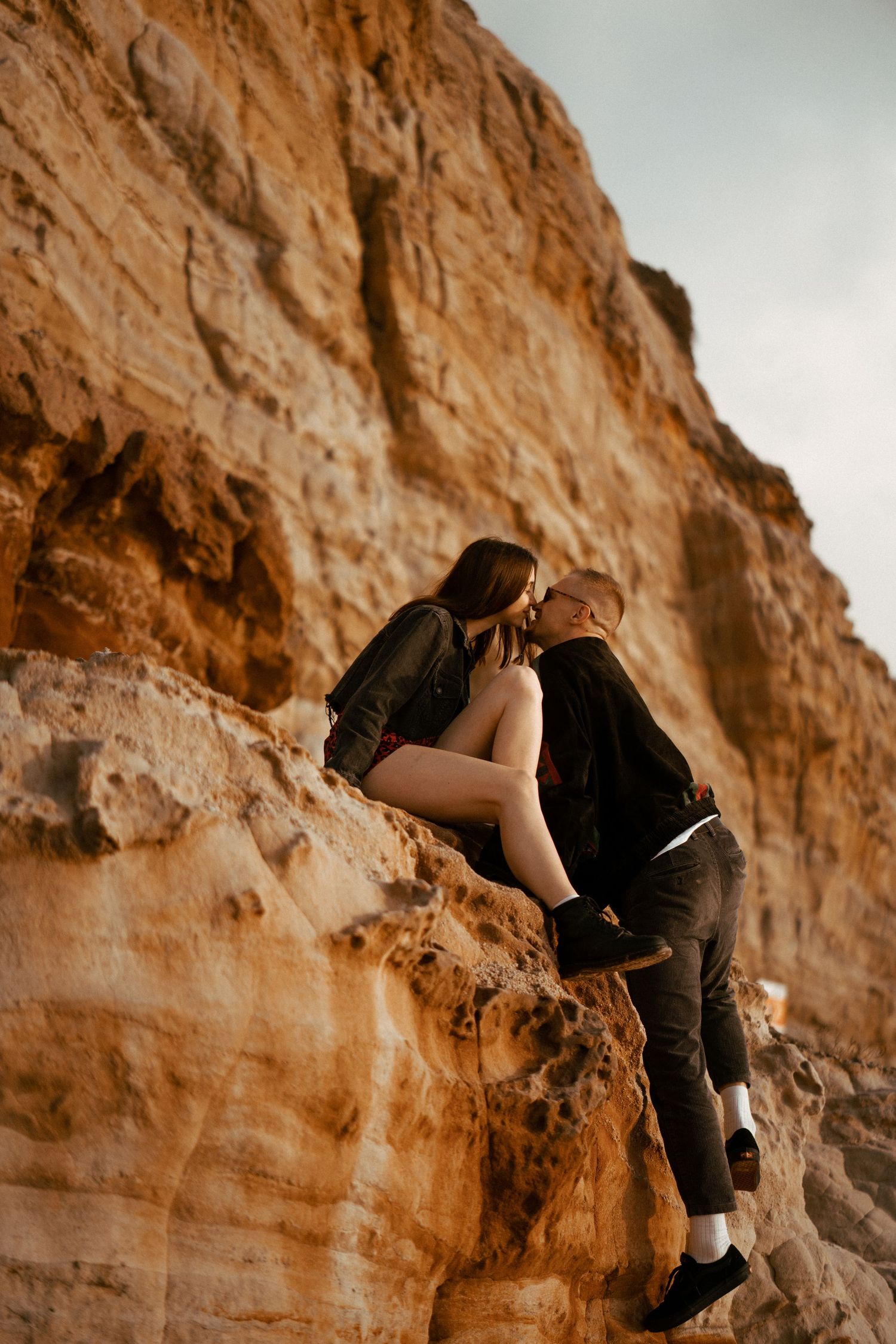 A couple climbing together on orange coastal rocks during a couples photography session in Portugal