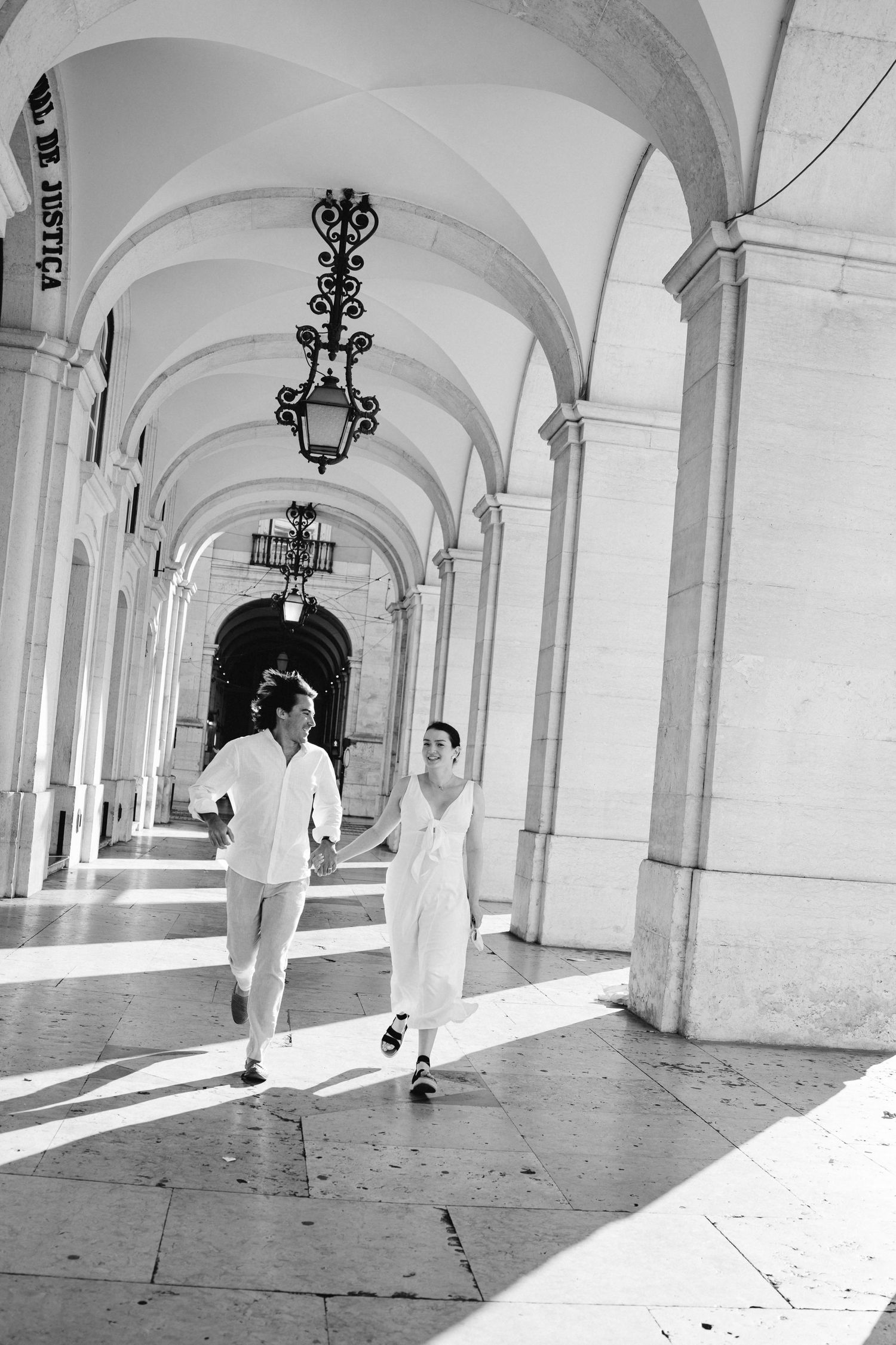 A couple running playfully through a grand colonnade with arched ceilings.