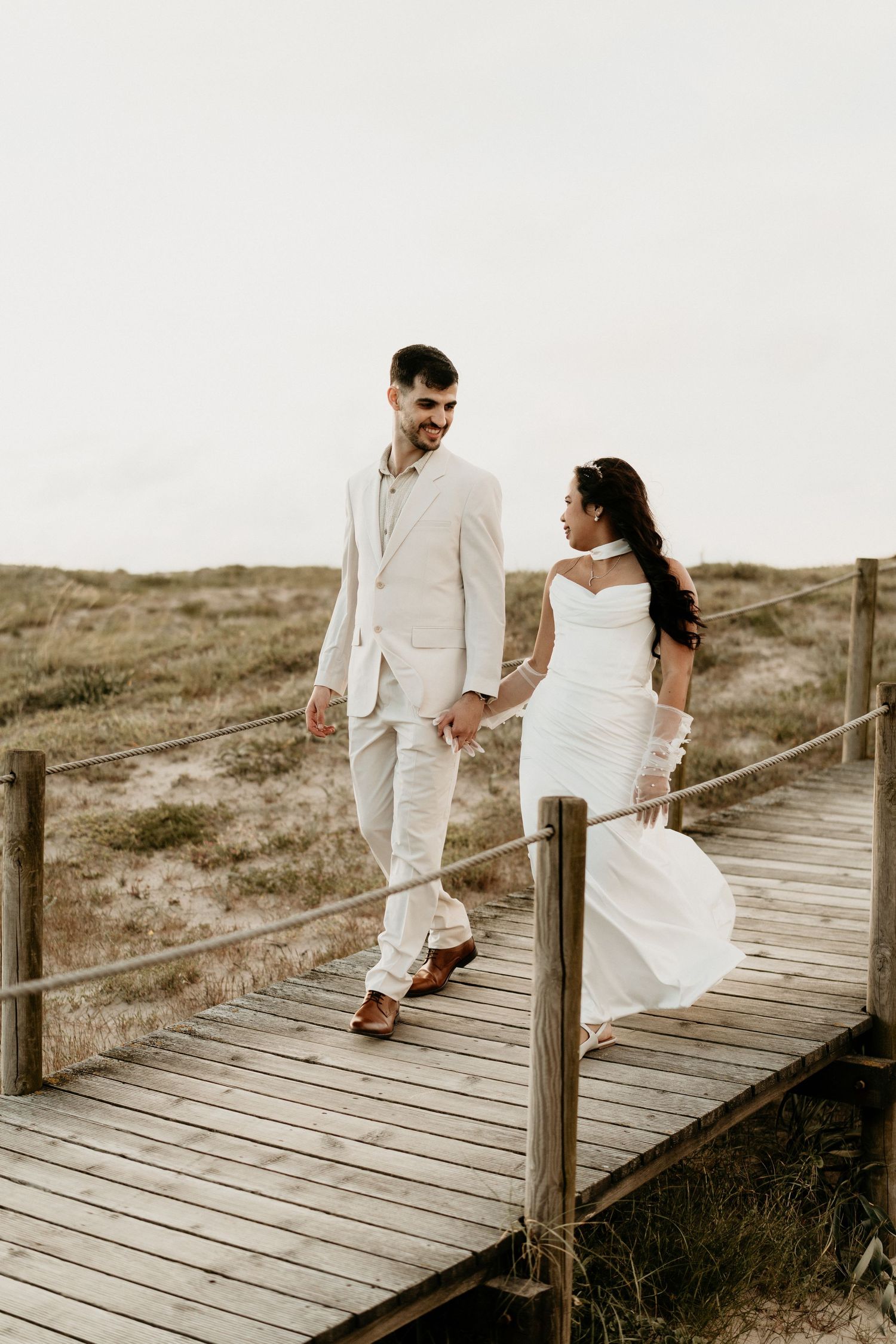 Bride and groom walking hand in hand on coastal boardwalk, destination wedding photographer Portugal