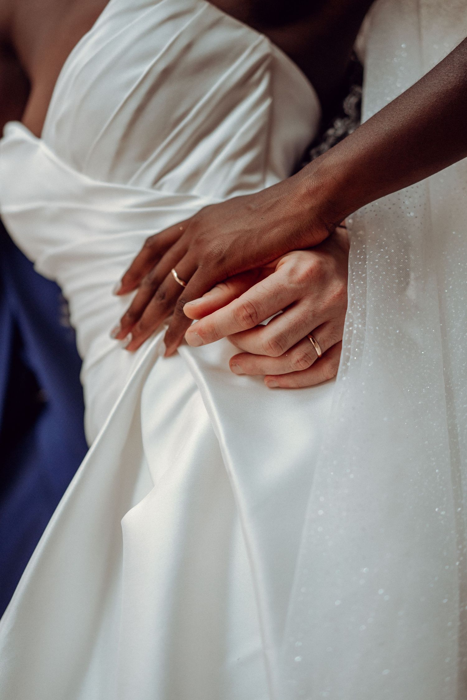 A close-up detail of a bride and groom holding hands with her wedding dress during their wedding in Portugal