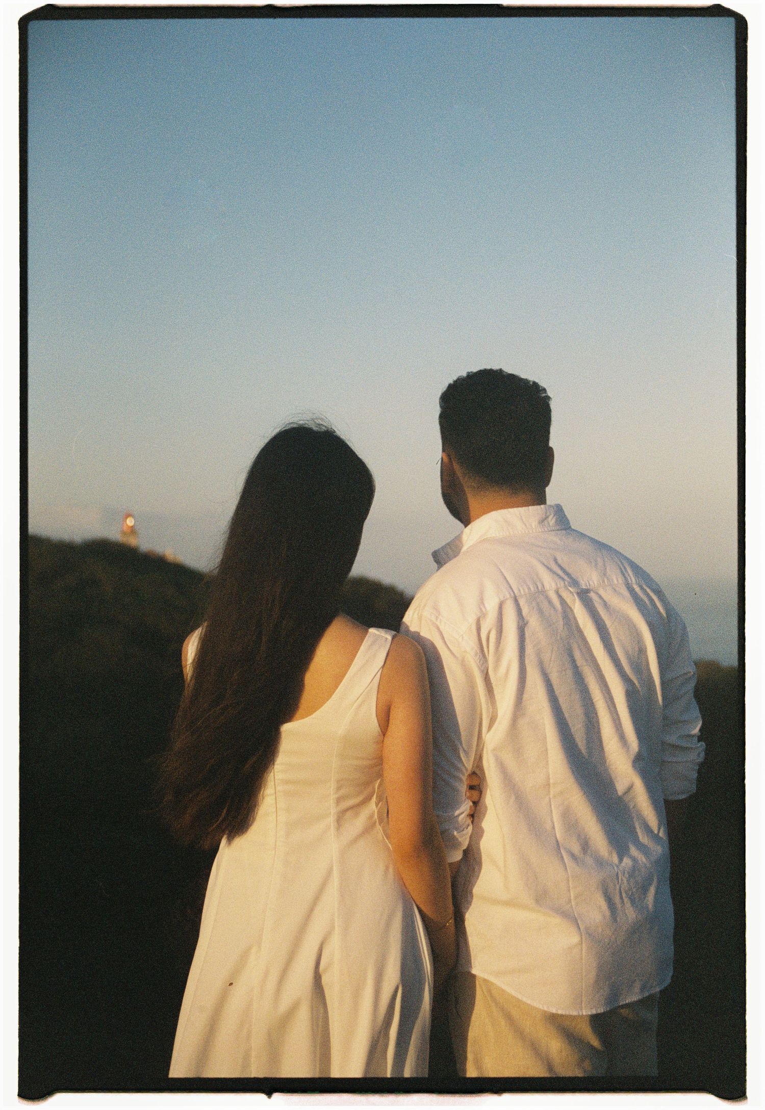A couple in white clothing viewing a sunset together from a hilltop.