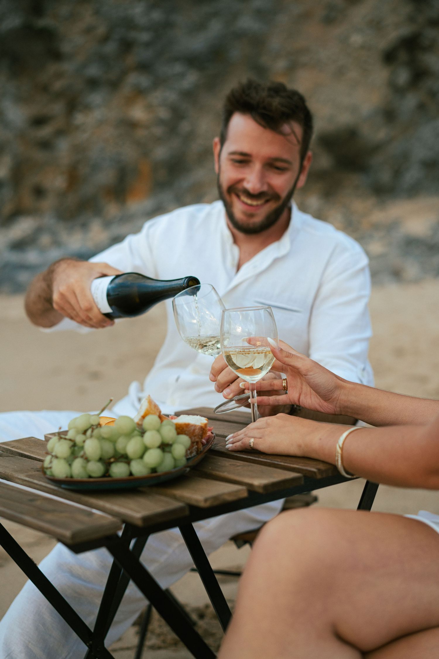A couple celebrating with champagne and a picnic on Praia da Adraga during their wedding portraits session in Portugal