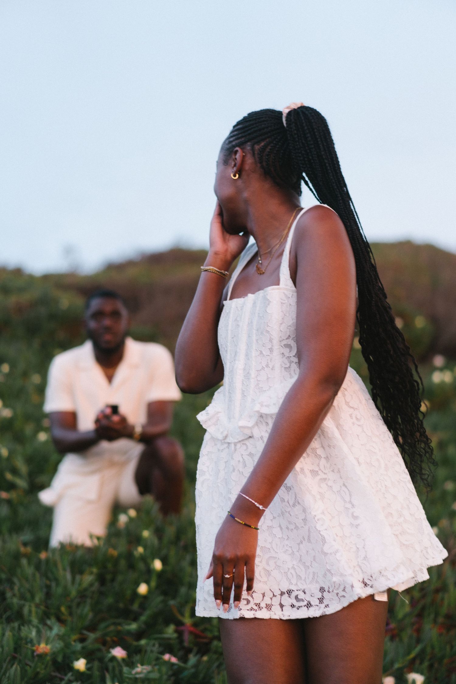 A couple standing together in the wildflowers on the clifftops above Praia da Ursa during a surprise proposal session in Portugal