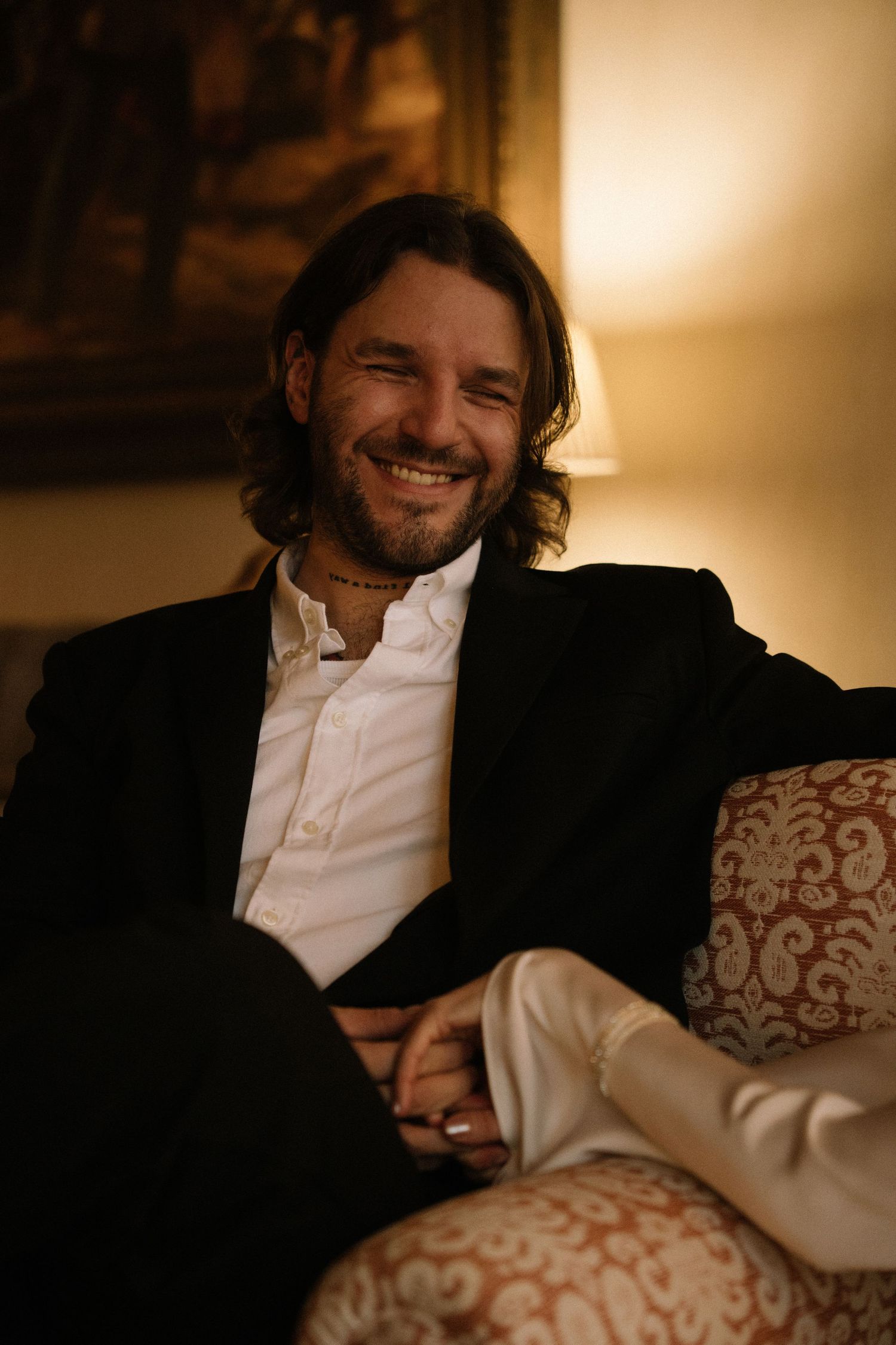 Groom laughing in vintage hotel armchair, candid elopement photography Portugal