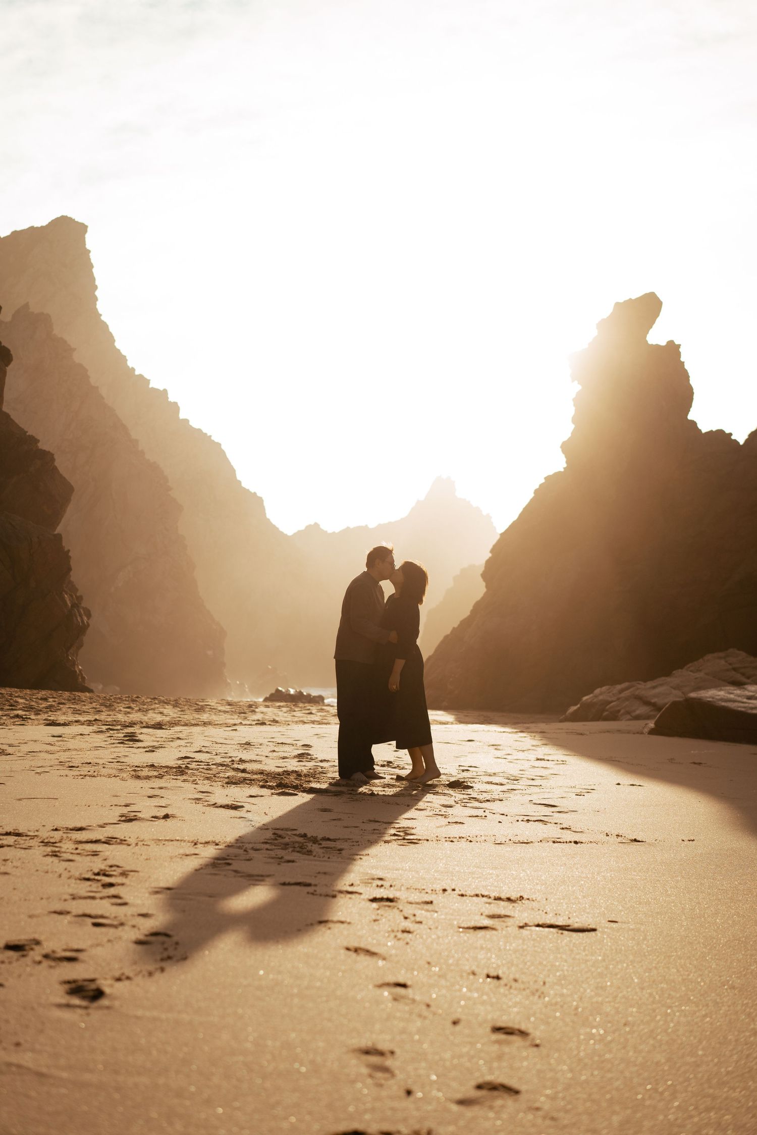 A couple silhouetted against golden light between the dramatic rock formations on Praia da Ursa, Portugal