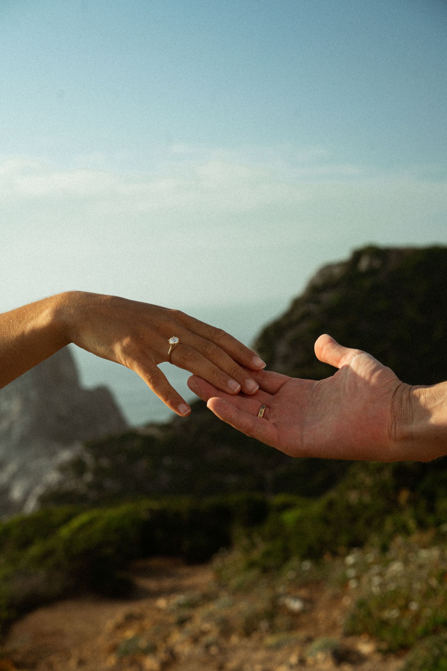 A close-up of a couple's hands with a wedding ring on the clifftops above Praia da Ursa, Portugal