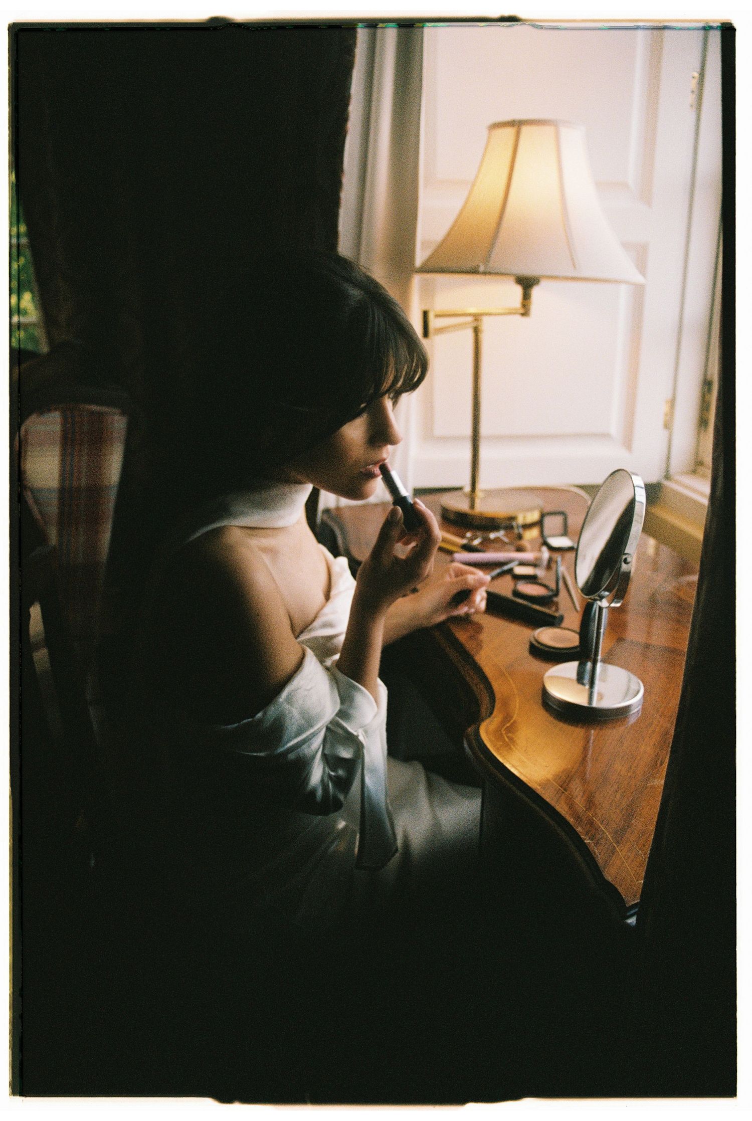 A film photograph of a bride having her makeup done in a warmly lit room during wedding morning preparations in Portugal