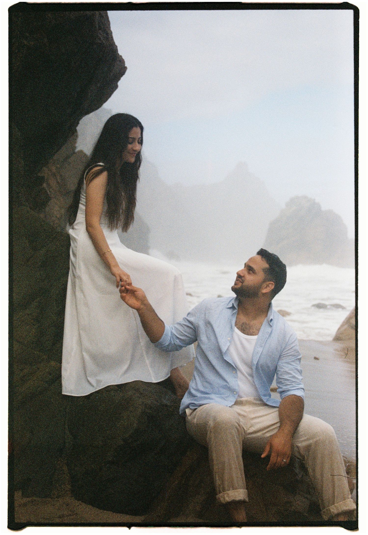 A film photograph of a couple sitting together on coastal rocks with ocean waves behind them in Portugal