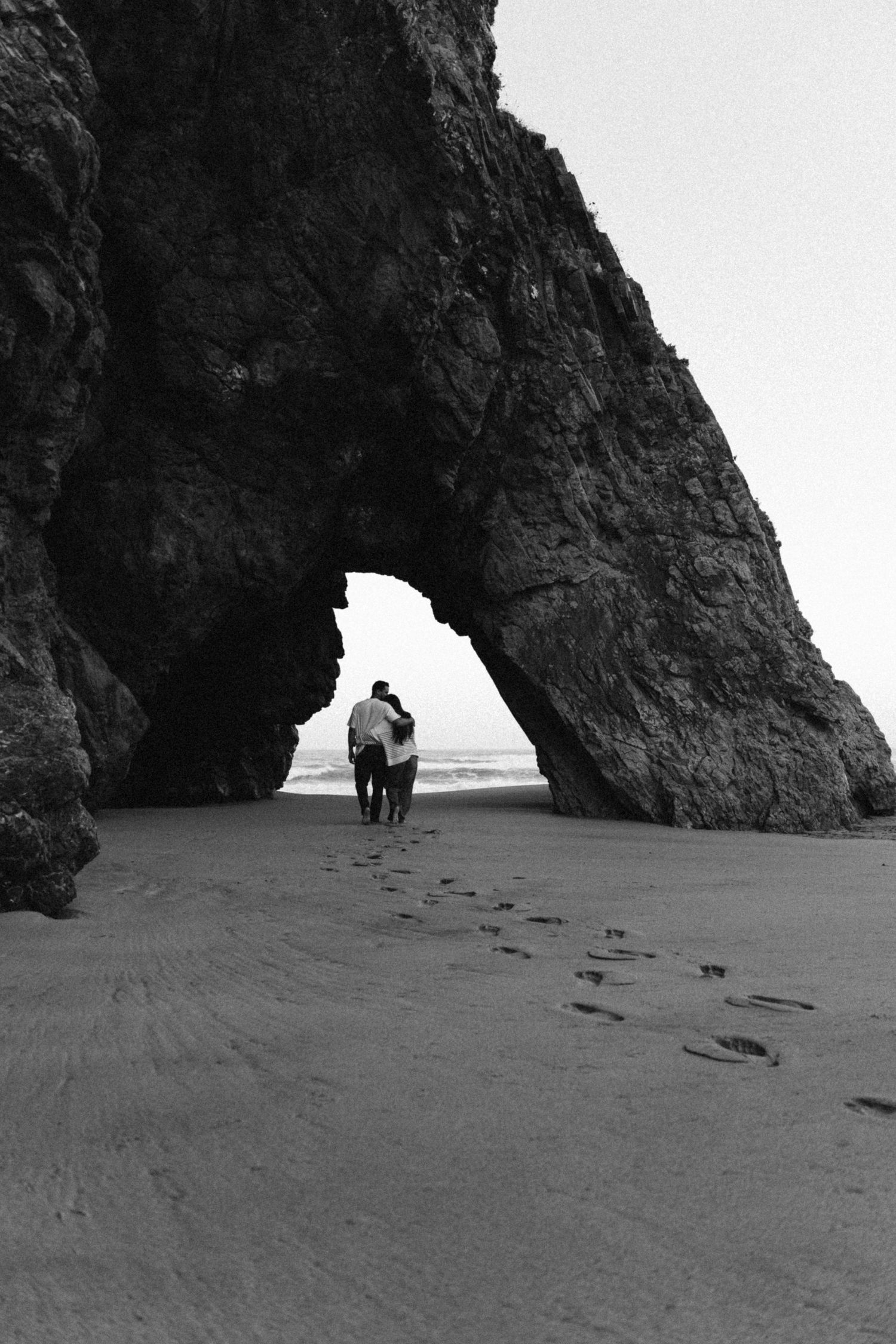A couple walking through a natural rock arch on Adraga beach in Portugal during a couples photography session