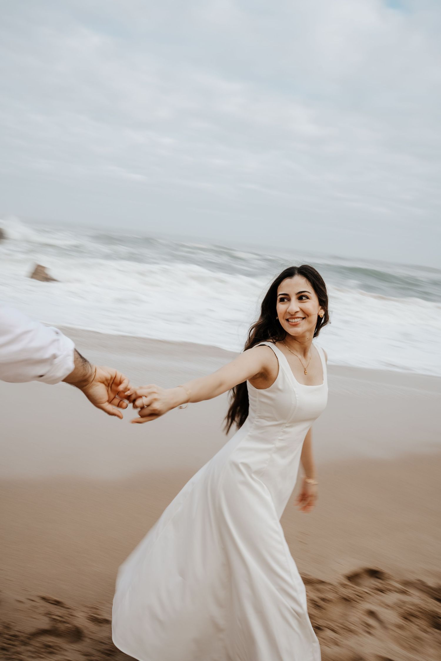 A woman in a white dress twirling joyfully on a beach with dramatic cliffs behind her in Portugal