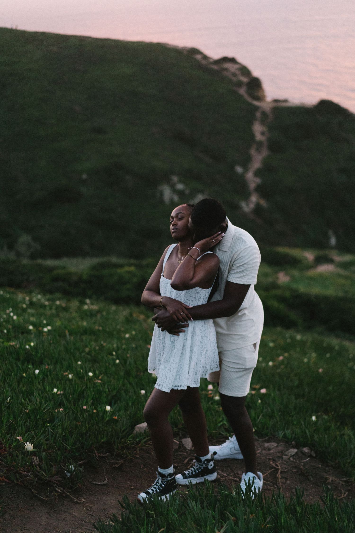 A couple embracing in the wildflowers on the clifftops above Praia da Ursa, Portugal