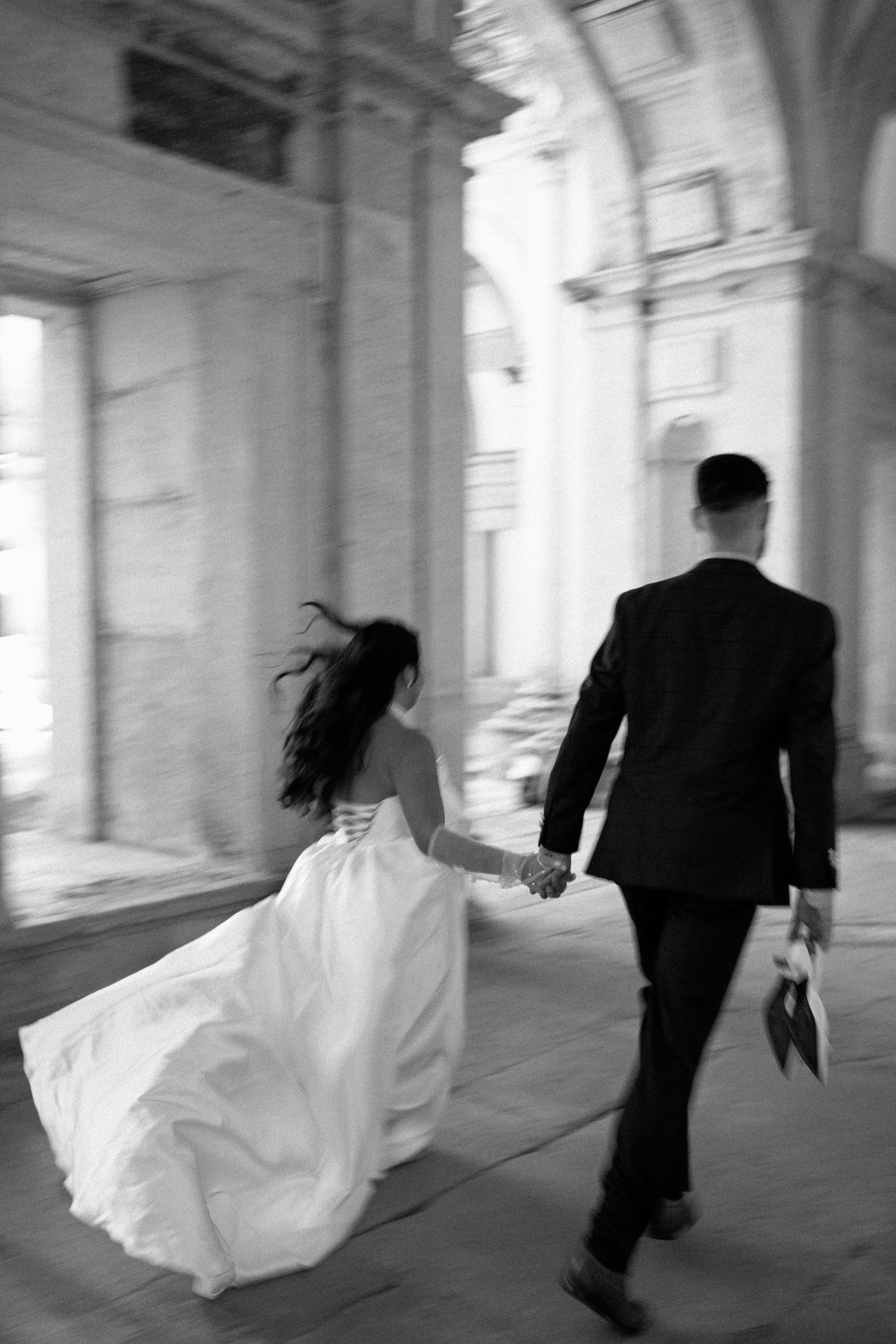 A couple running playfully through a grand colonnade during their pre-wedding session in Portugal