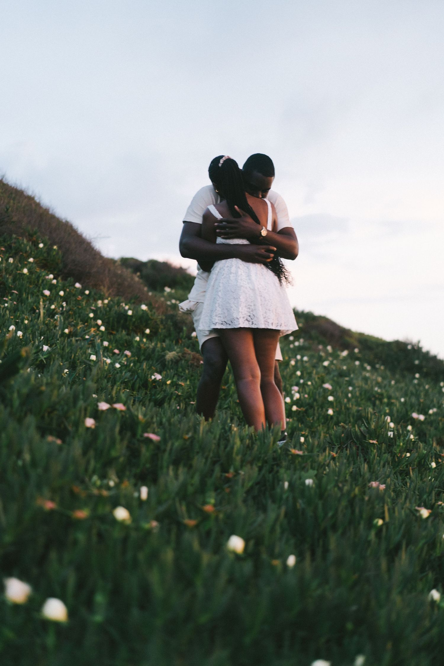 A couple embracing in the wildflowers on the cliffs overlooking Praia da Ursa after a surprise proposal in Portugal