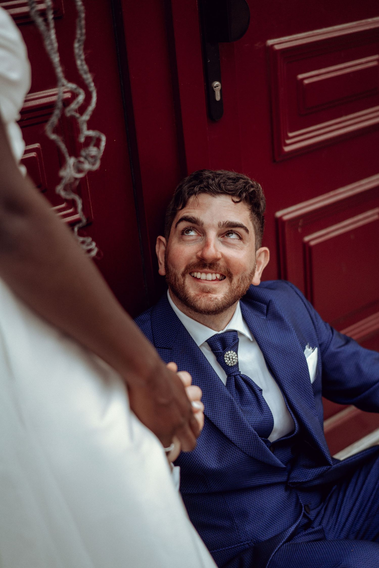 A candid portrait of a groom laughing on the steps of a historic building during his wedding in Portugal