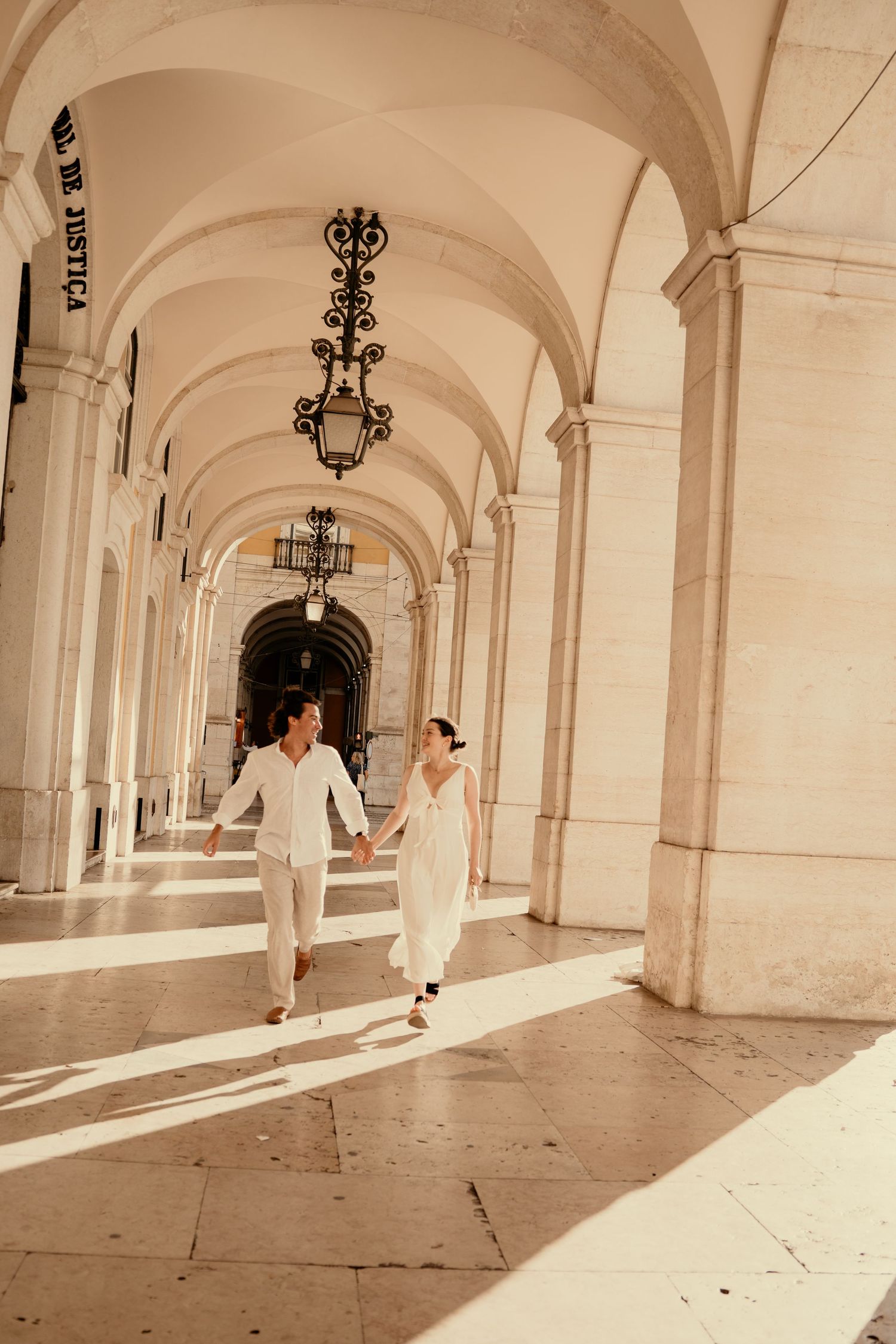 A couple walking hand in hand through a grand arched colonnade during their elopement in Lisbon, Portugal