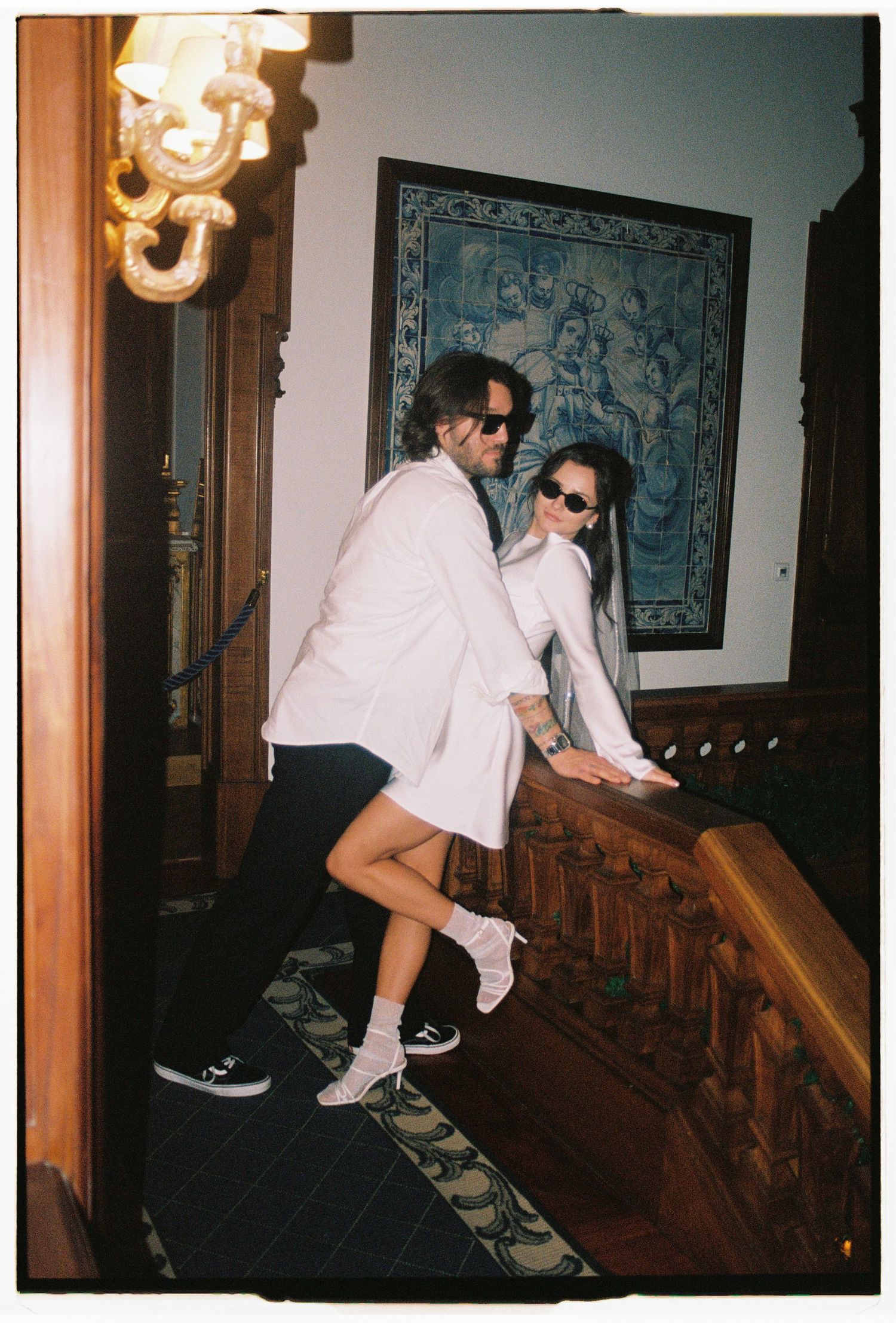 Bride sitting on hotel staircase railing in sunglasses, film photography elopement Lisbon Portugal
