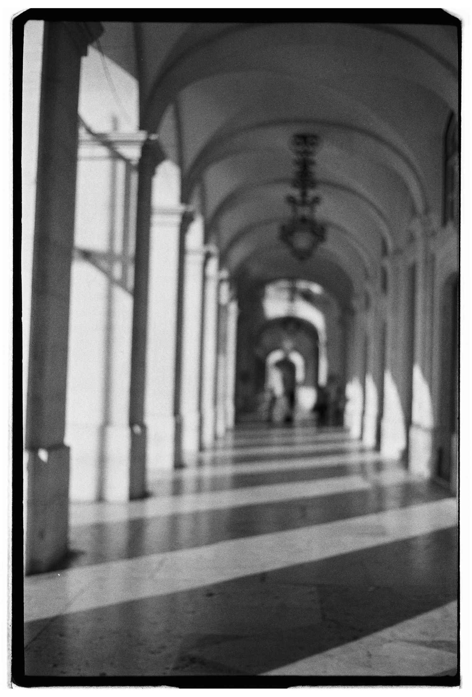 A black and white film photograph of a grand arched corridor in Lisbon
