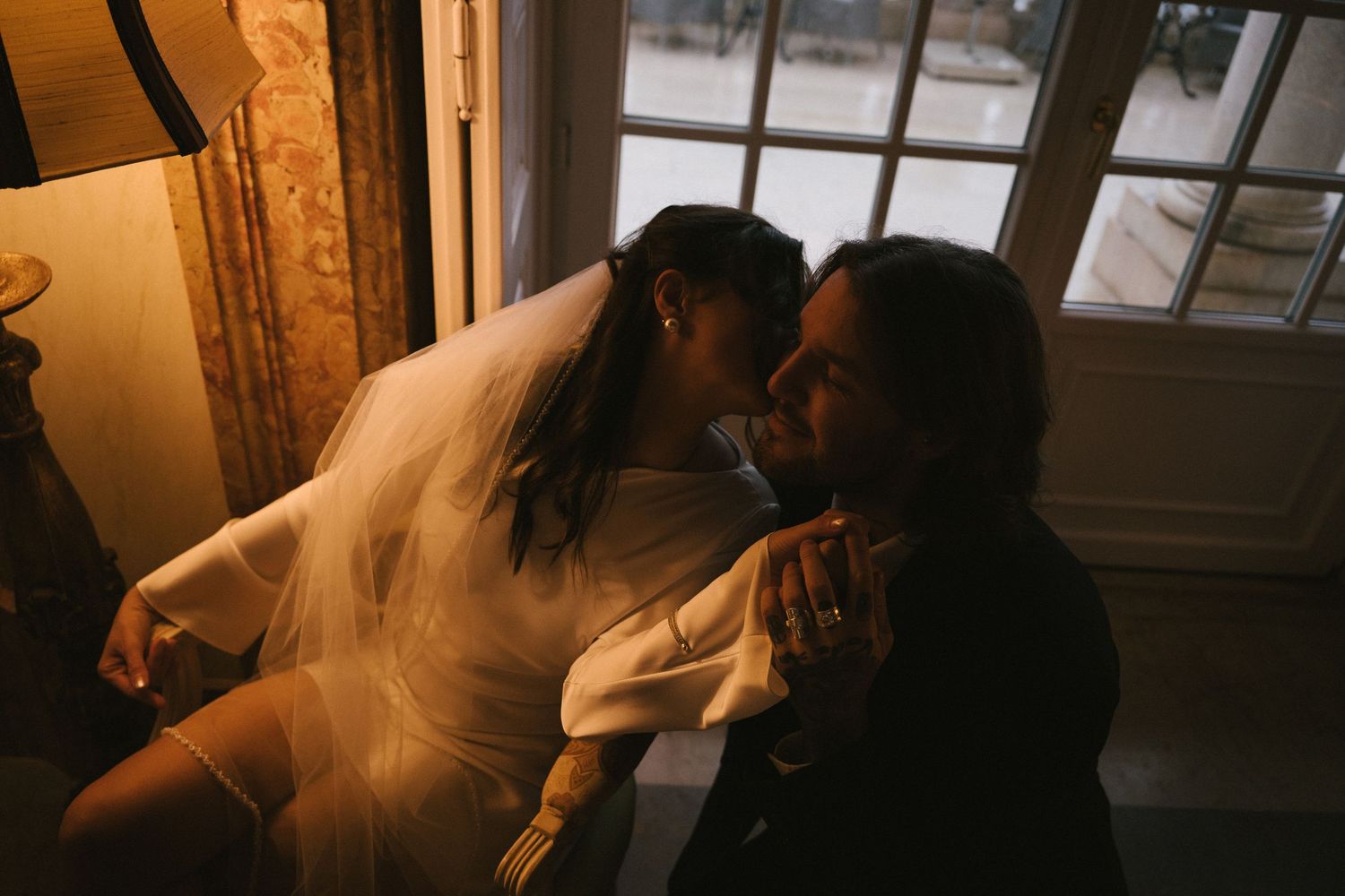 A couple sharing a tender moment by a window in warm indoor light during their elopement session in Estoril Vintage Hotel